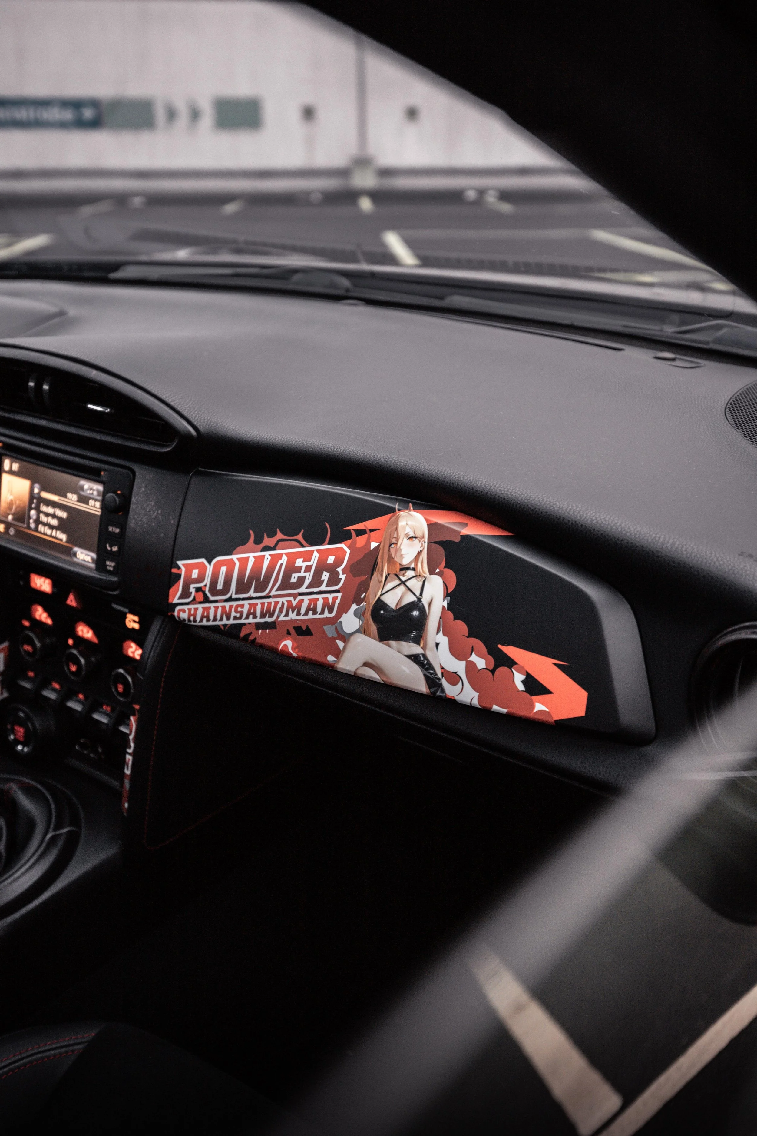 Innensicht eines Autos mit einem Aufkleber auf der Beifahrertür, der ein Anime-Charakter und den Text 'POWER CHAINSAW MAN' zeigt.
