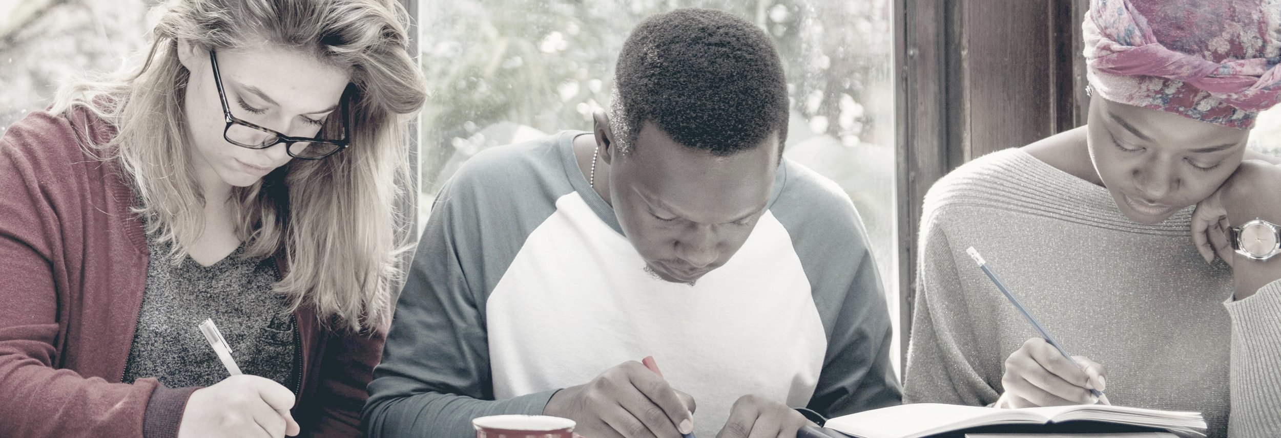 Three international students concentrating on their language studies and writing in their notebooks.