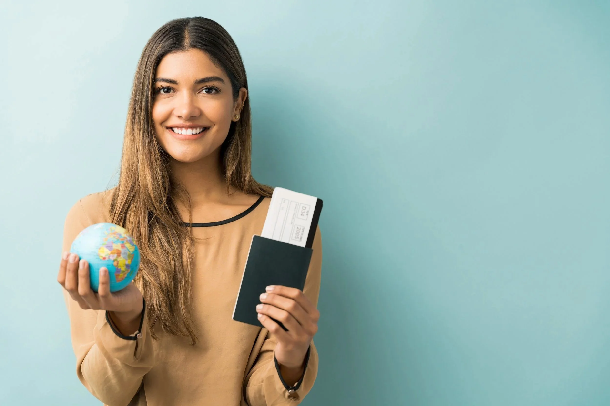happy-young-woman-holding-passport-boarding-pass-with-globe-while-standing-against-blue-background.jpg