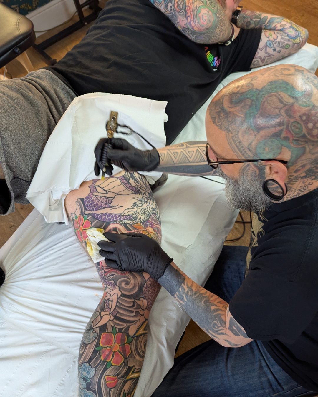 steve doing a tattoo on someones leg as part of a leg sleeve