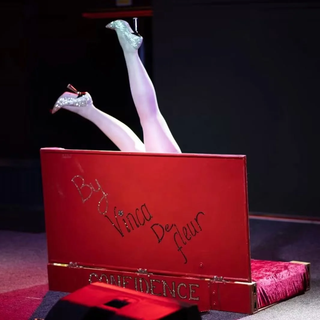 A red giant book with handwritten text, and two high-heeled legs with glittery shoes and stockings emerging from it.