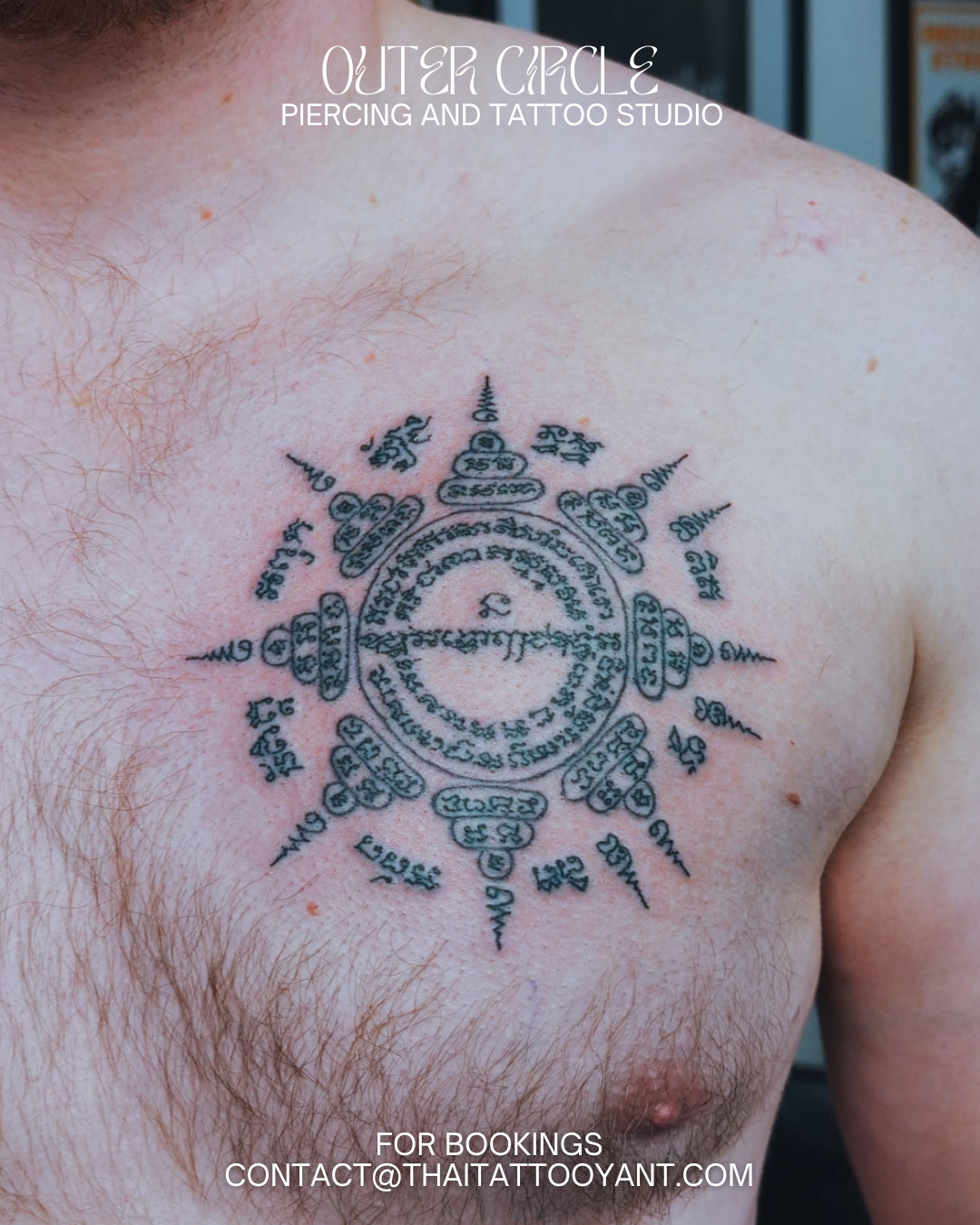 Sak Yant traditional thai tattoo Black tattoo of a spiritual symbol with intricate patterns and script, located on the upper left chest of a person with light skin and chest hair, against a slightly blurred background.