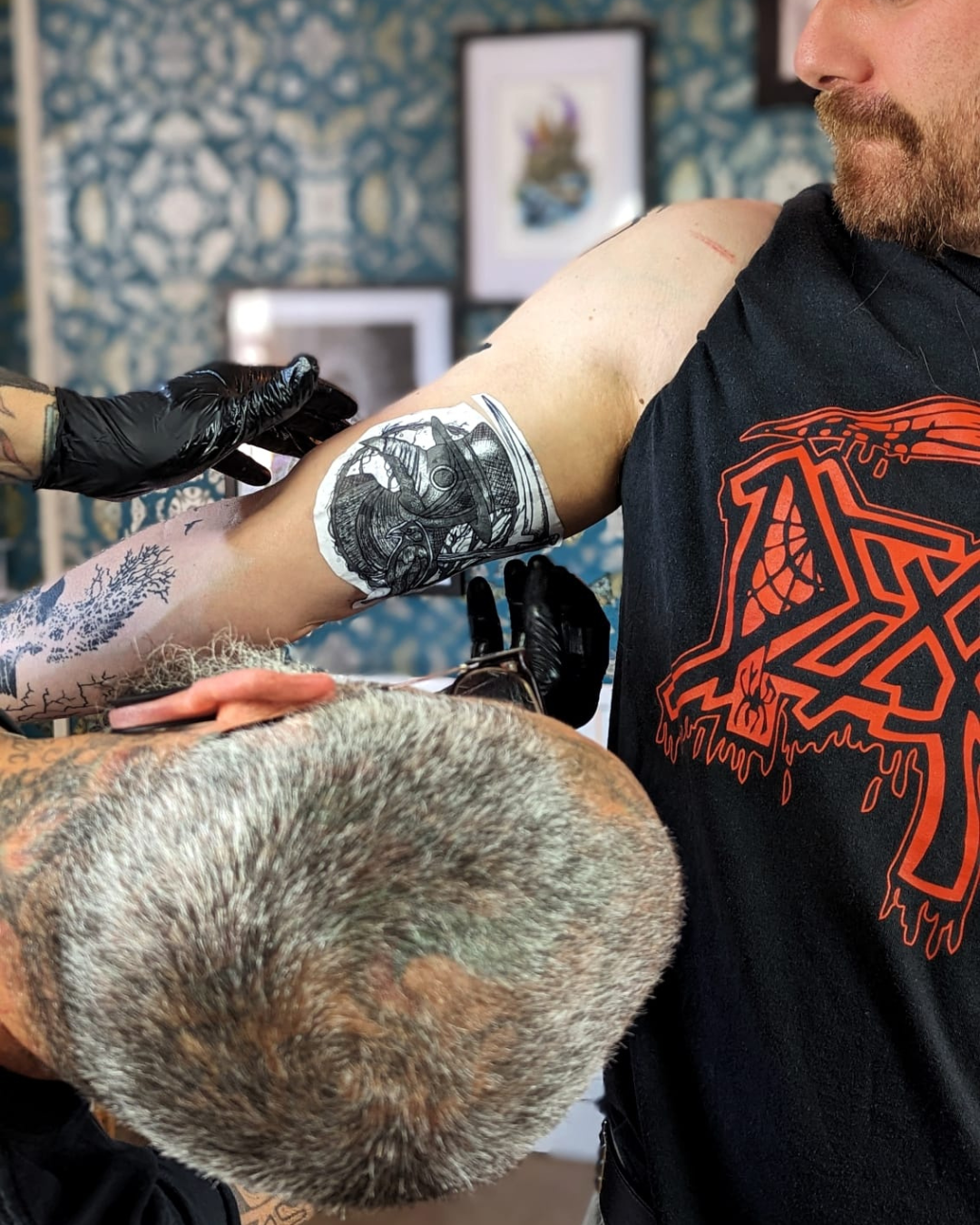 Man getting a tattoo stencil placed on his upper arm with a tattoo artist.