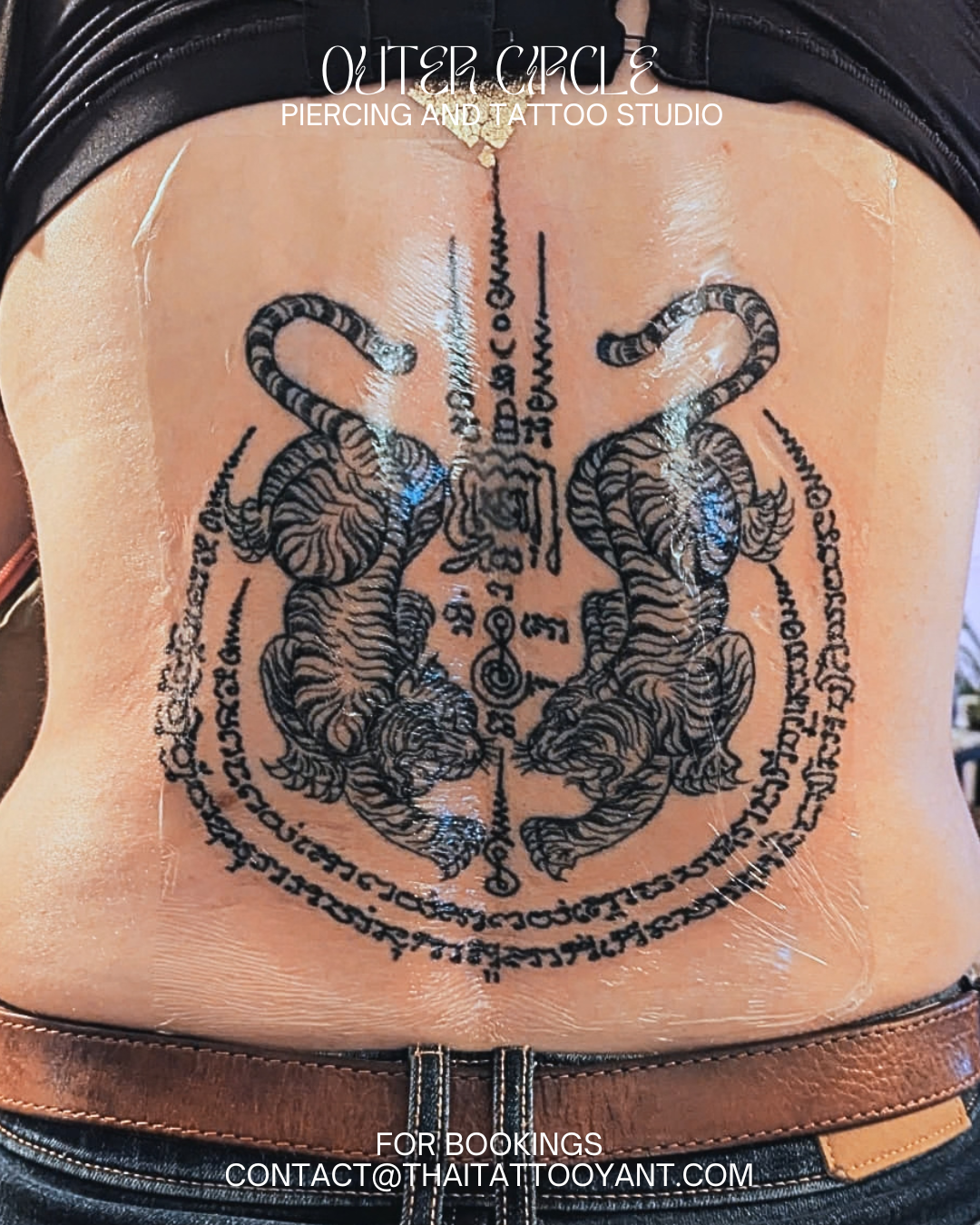 Sak Yant Thai tattoo of two tigers facing each other with an oval border of text, located on a person's lower back