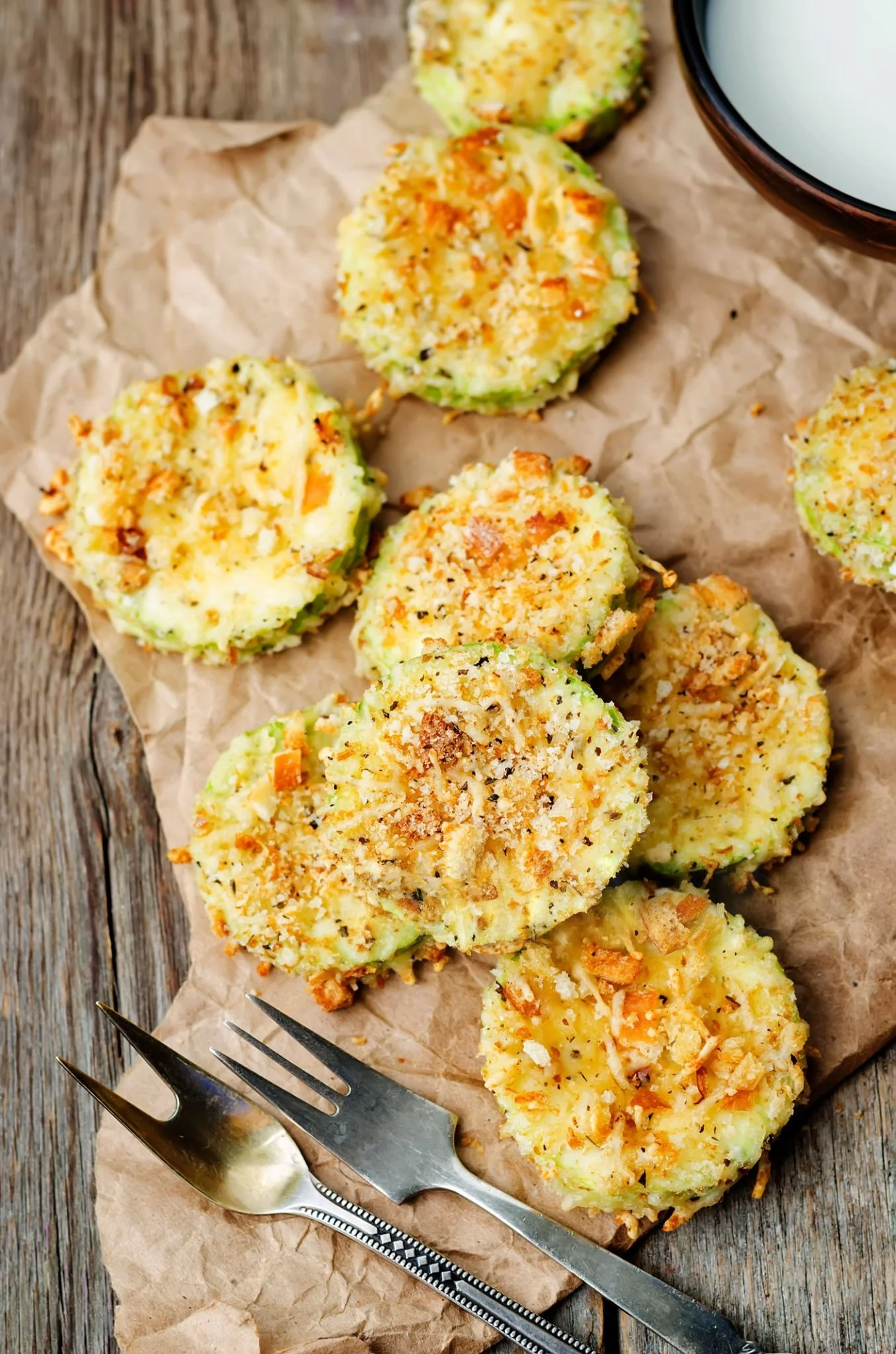 Baked stuffed zucchini slices topped with breadcrumbs, cheese, and herbs, arranged on crumpled parchment paper on a rustic wooden surface.