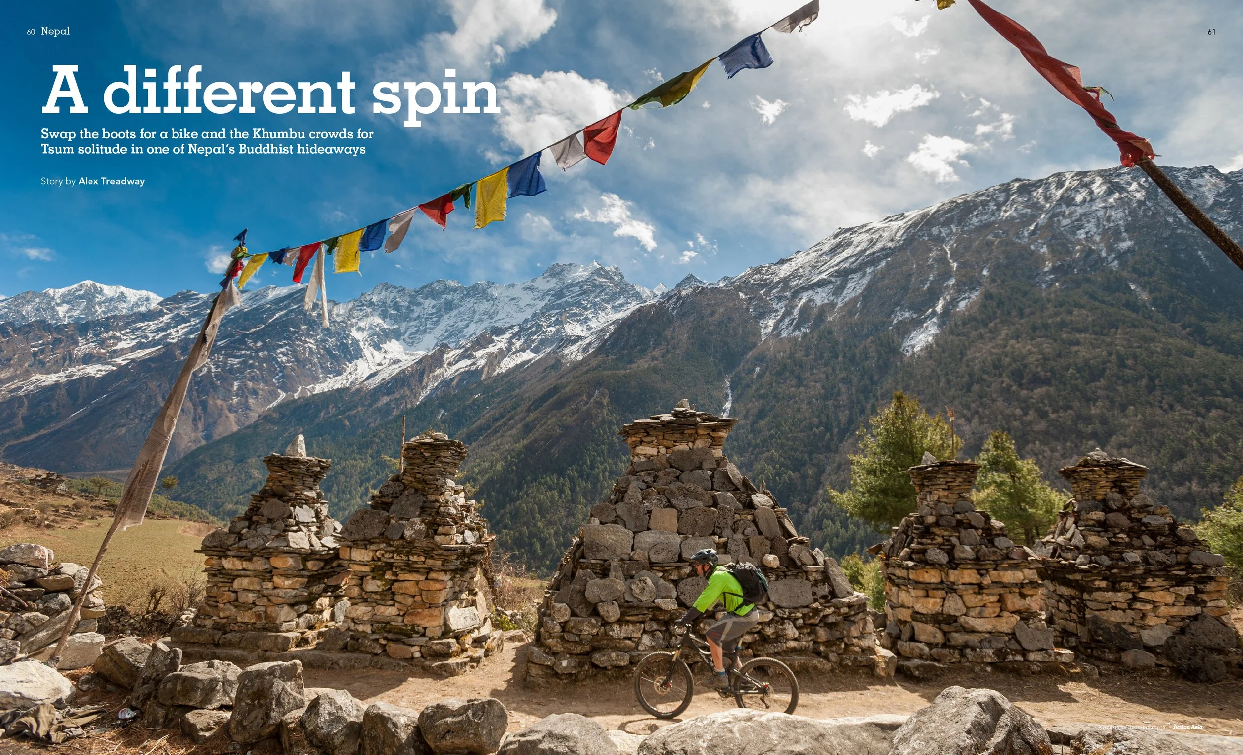 A mountain landscape with snow-capped peaks and blue sky, prayer flags hanging across the scene, stone stupas or monuments in the foreground, and a cyclist riding past.