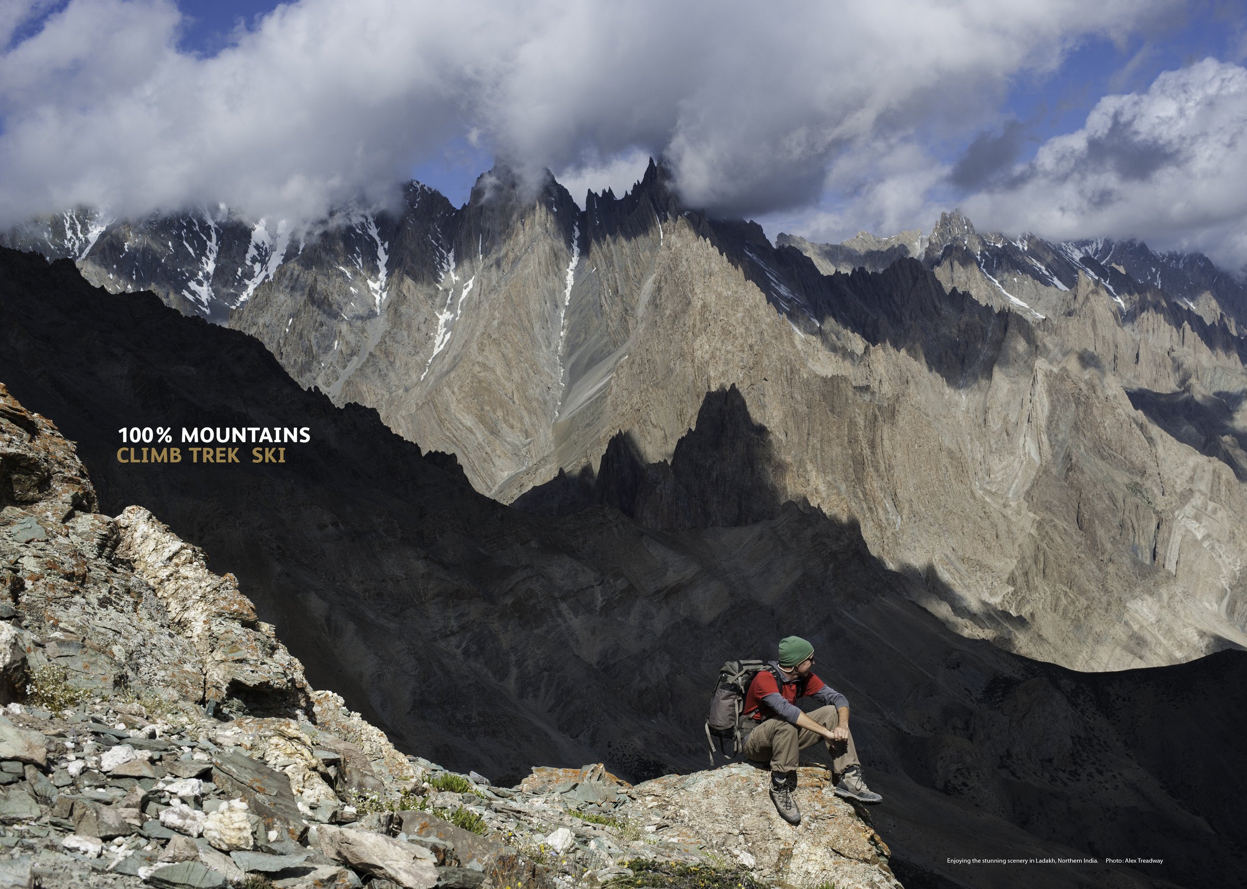 A person sitting on a rocky mountain terrain, surrounded by steep mountain peaks partially covered with snow, under a cloudy sky in Ladakh, Northern India.