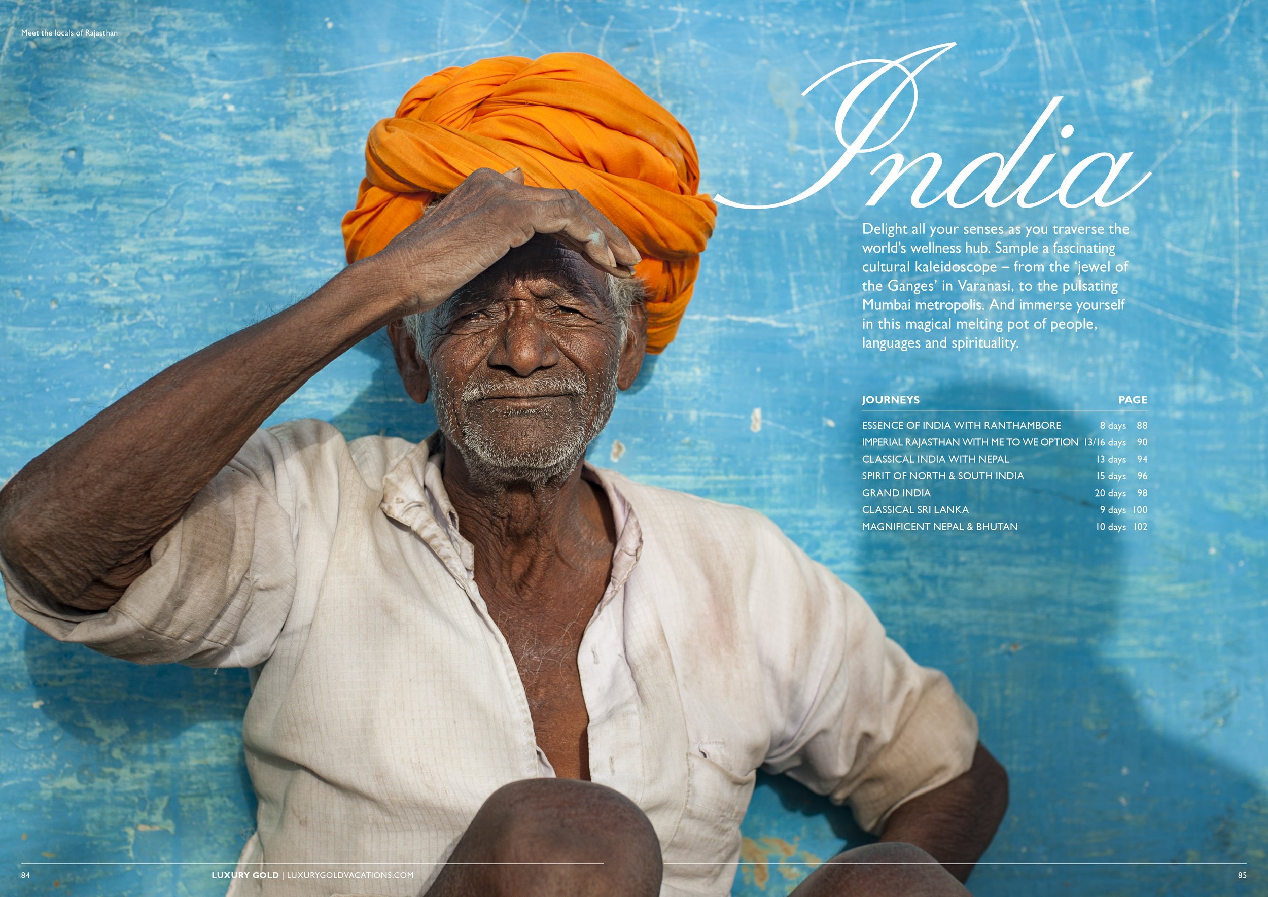 An elderly man with dark skin wearing an orange turban and a light-colored shirt, sitting against a blue textured wall. He has a relaxed expression and is shading his eyes with his right hand.