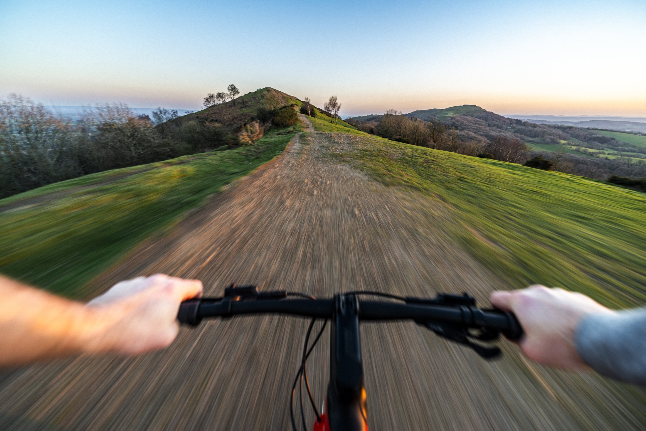 A bike is speeding along a trail on top of the Malvern Hills. The landscape is blurring as it speeds past. The image is taken from the rider's perspective (POV). 