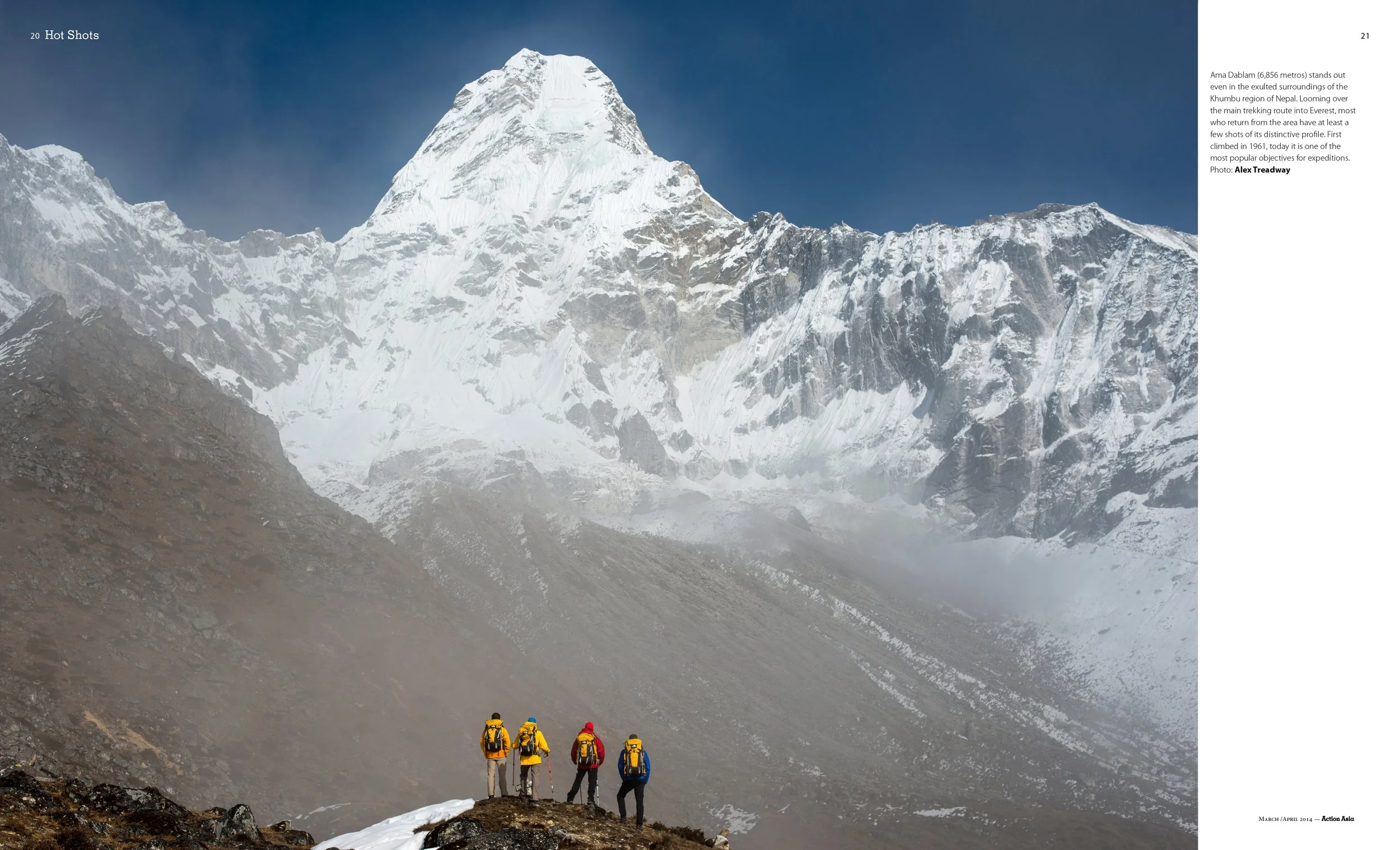 Four hikers with backpacks standing on rocky terrain, looking at a large, snow-covered mountain peak in the distance - Ama Dablam in Nepal.
