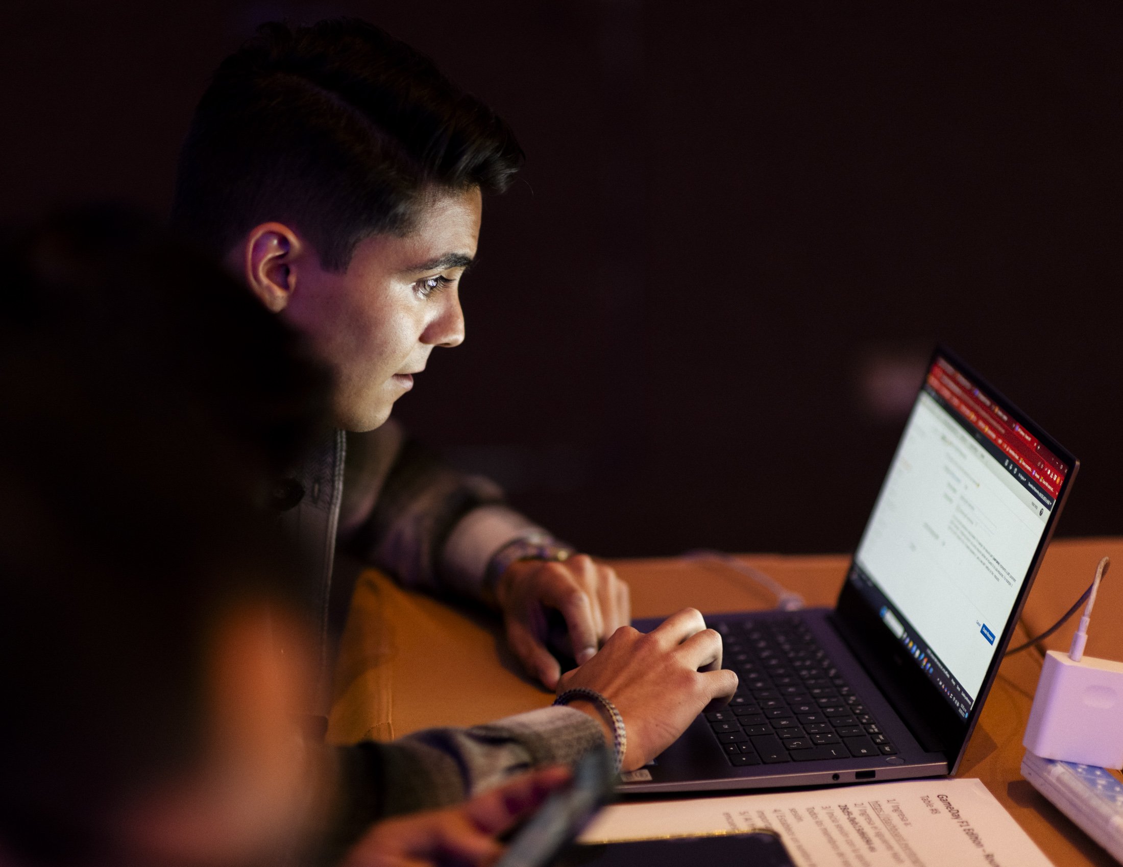 A man working on a computer in darkness with an intense expression on his face. 