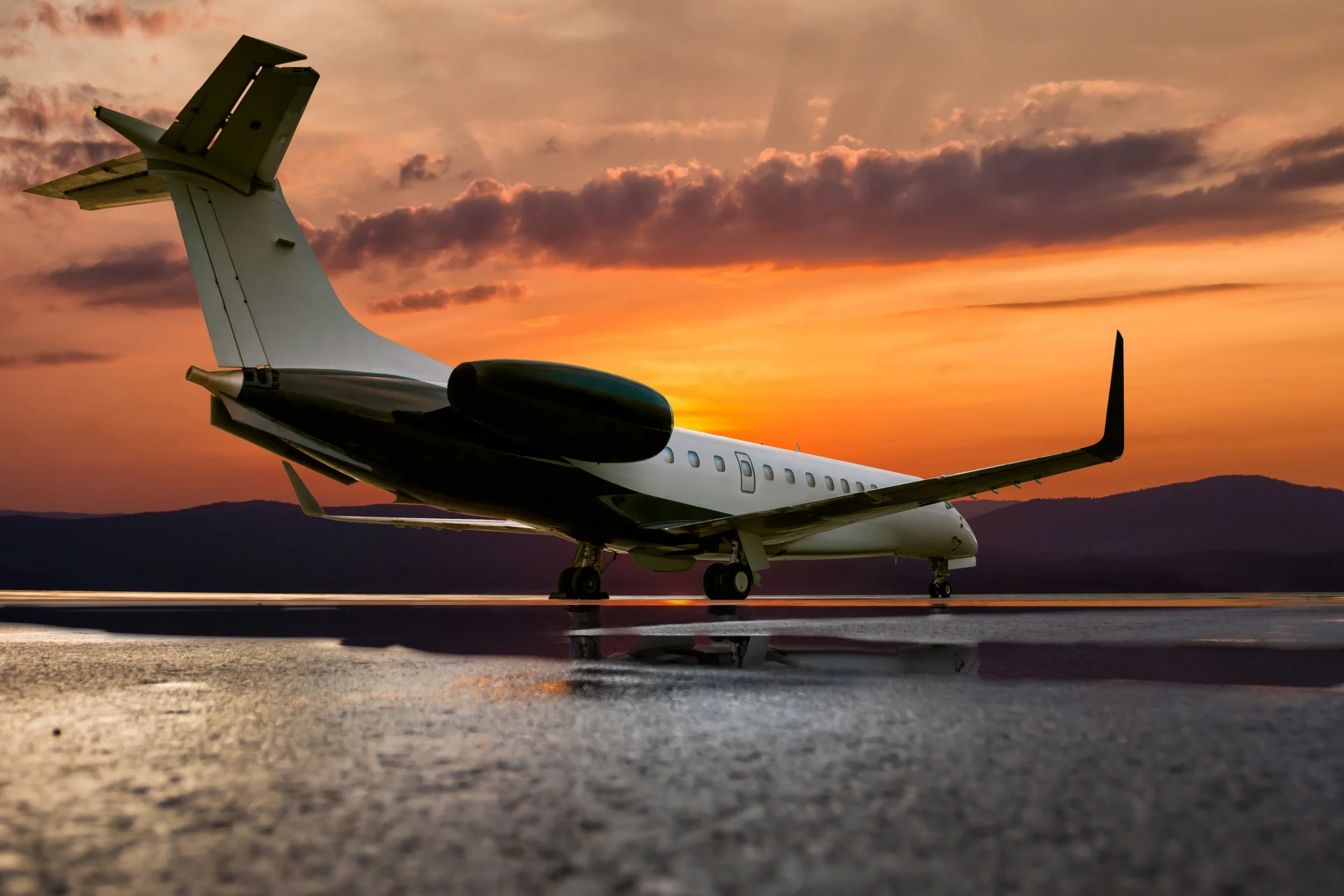 Private jet parked on runway during sunset with colorful sky and distant mountains in background.