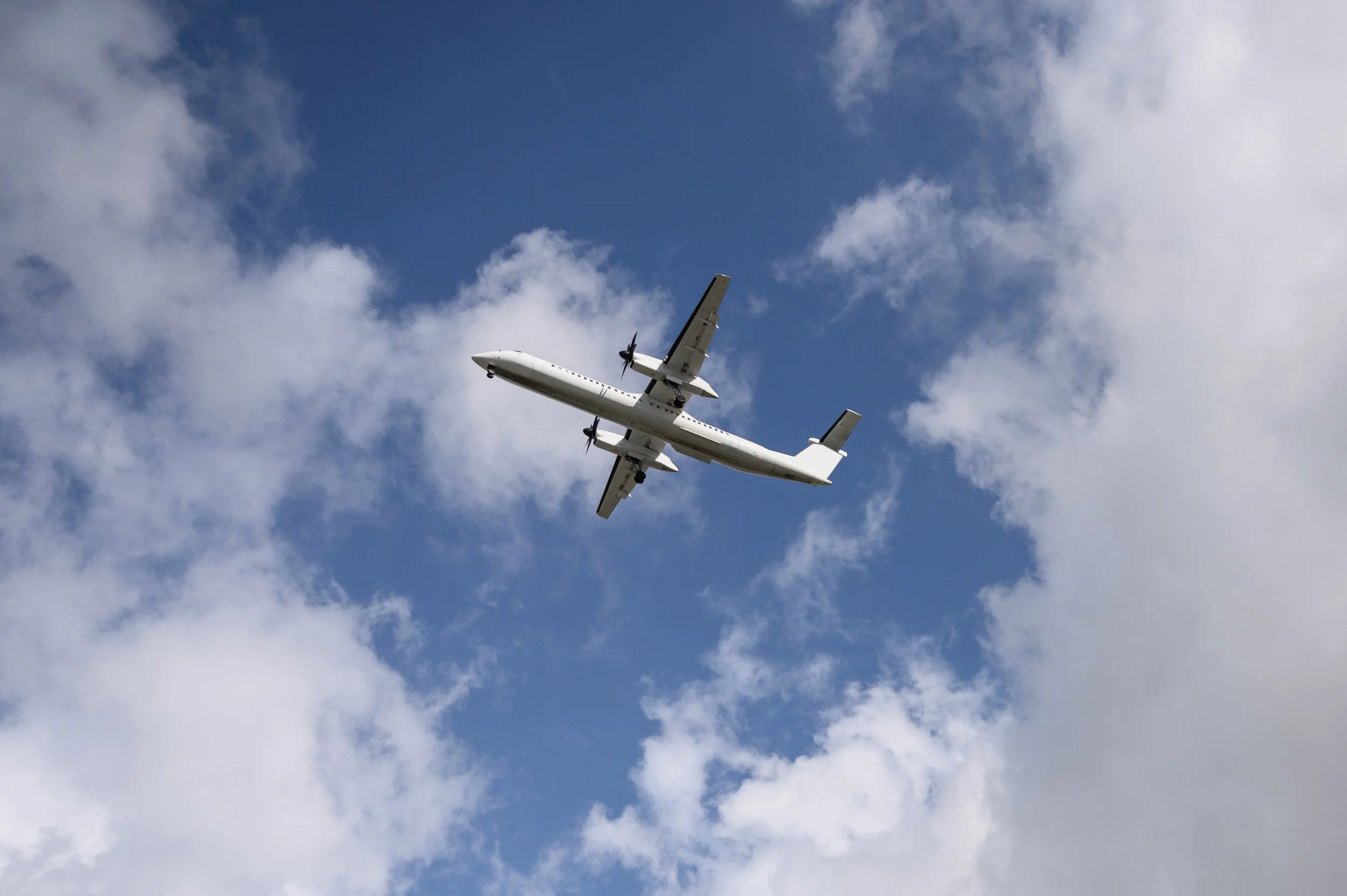 A white airplane flying through a partly cloudy blue sky.