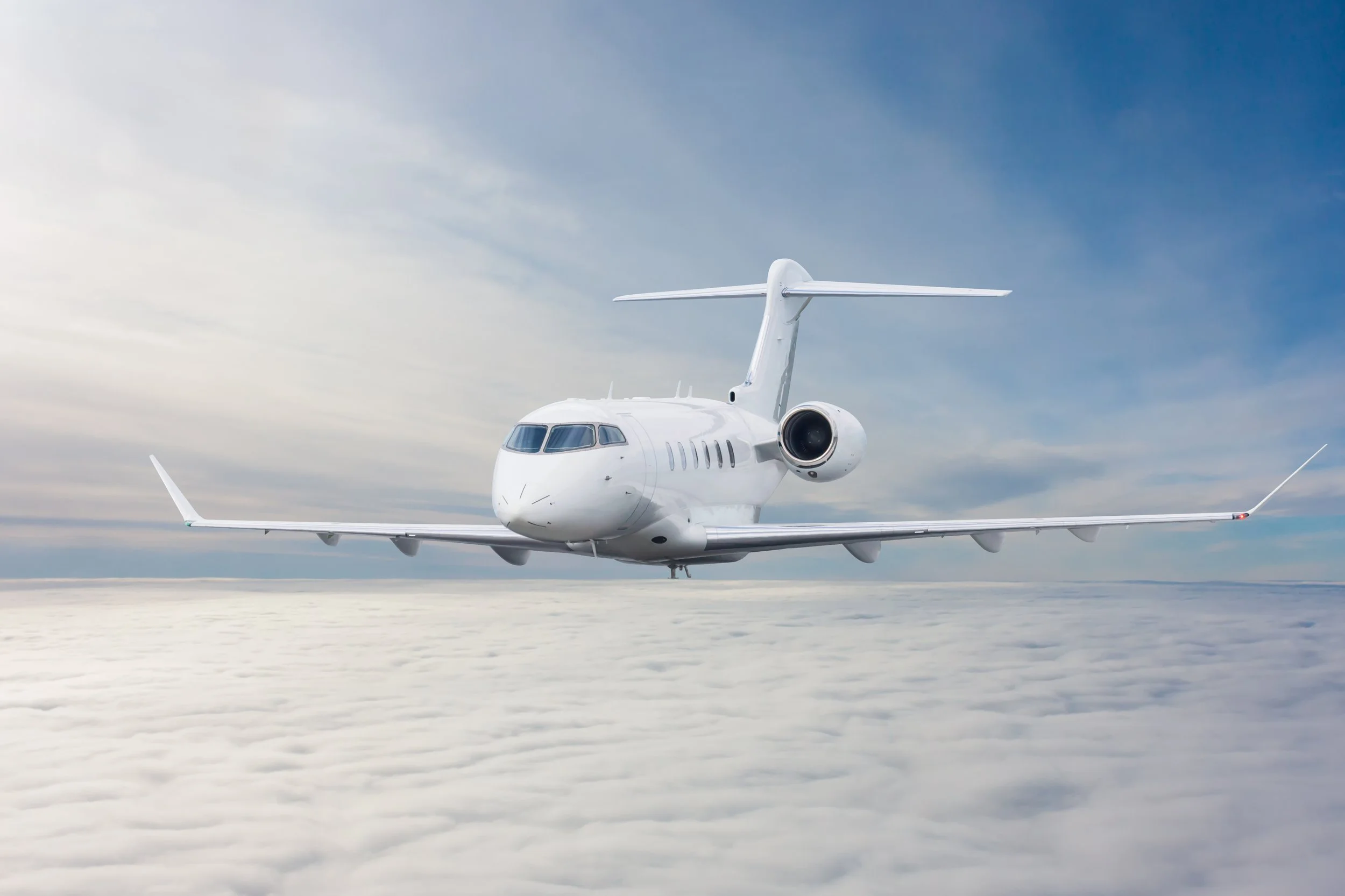 A white private jet flying above clouds in a clear sky.