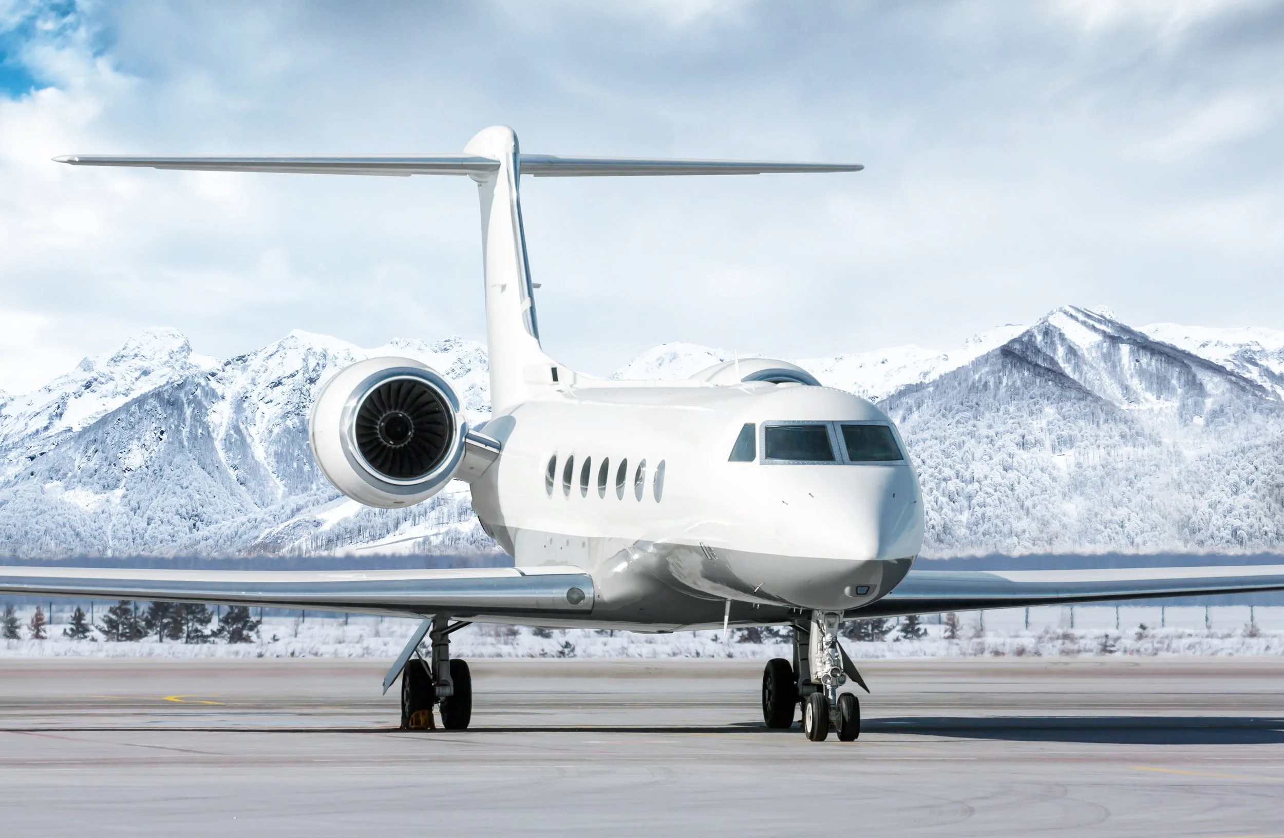 A white private jet on a runway in a snowy mountain landscape.
