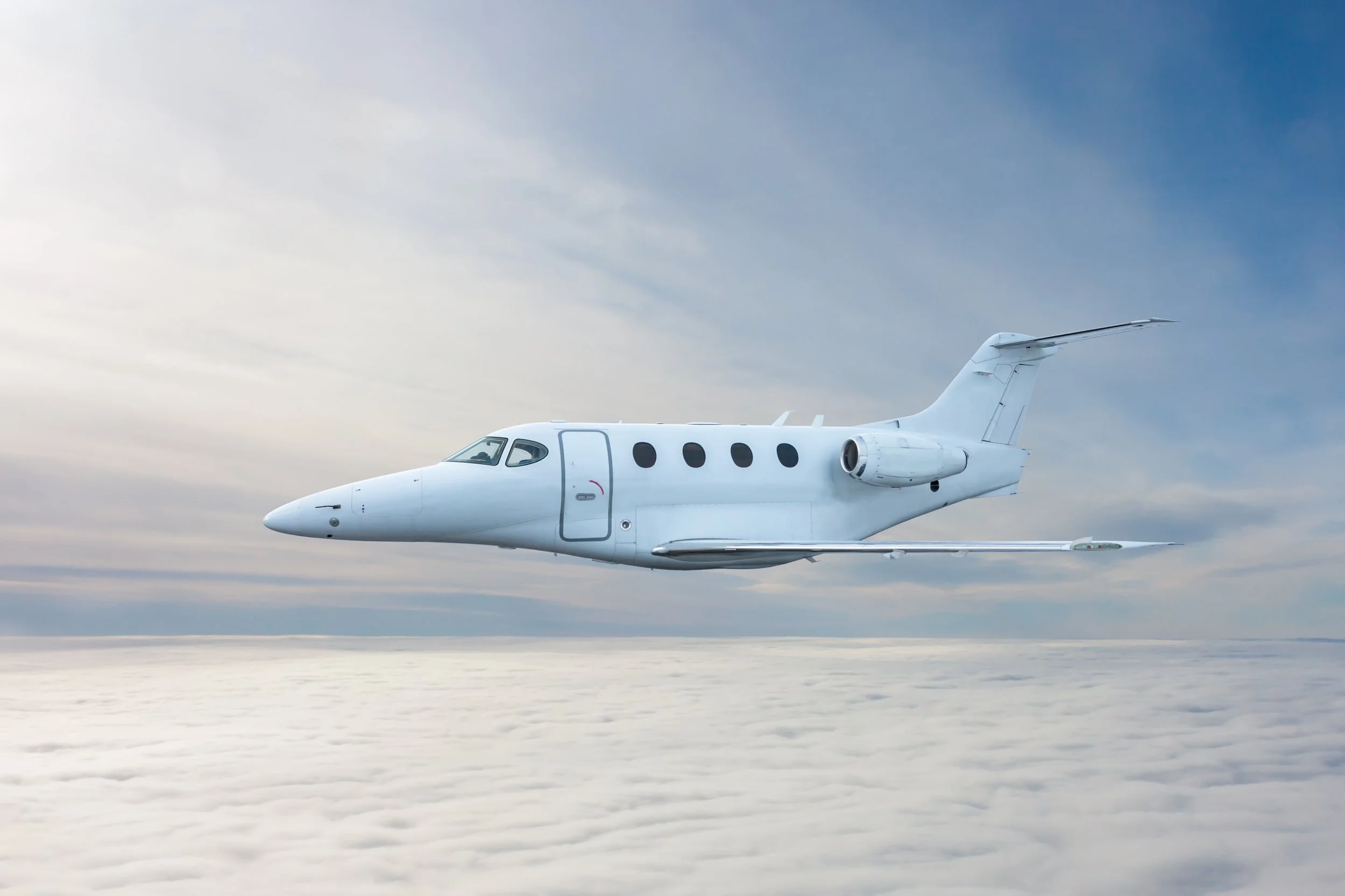 White private jet flying above the clouds in the sky.