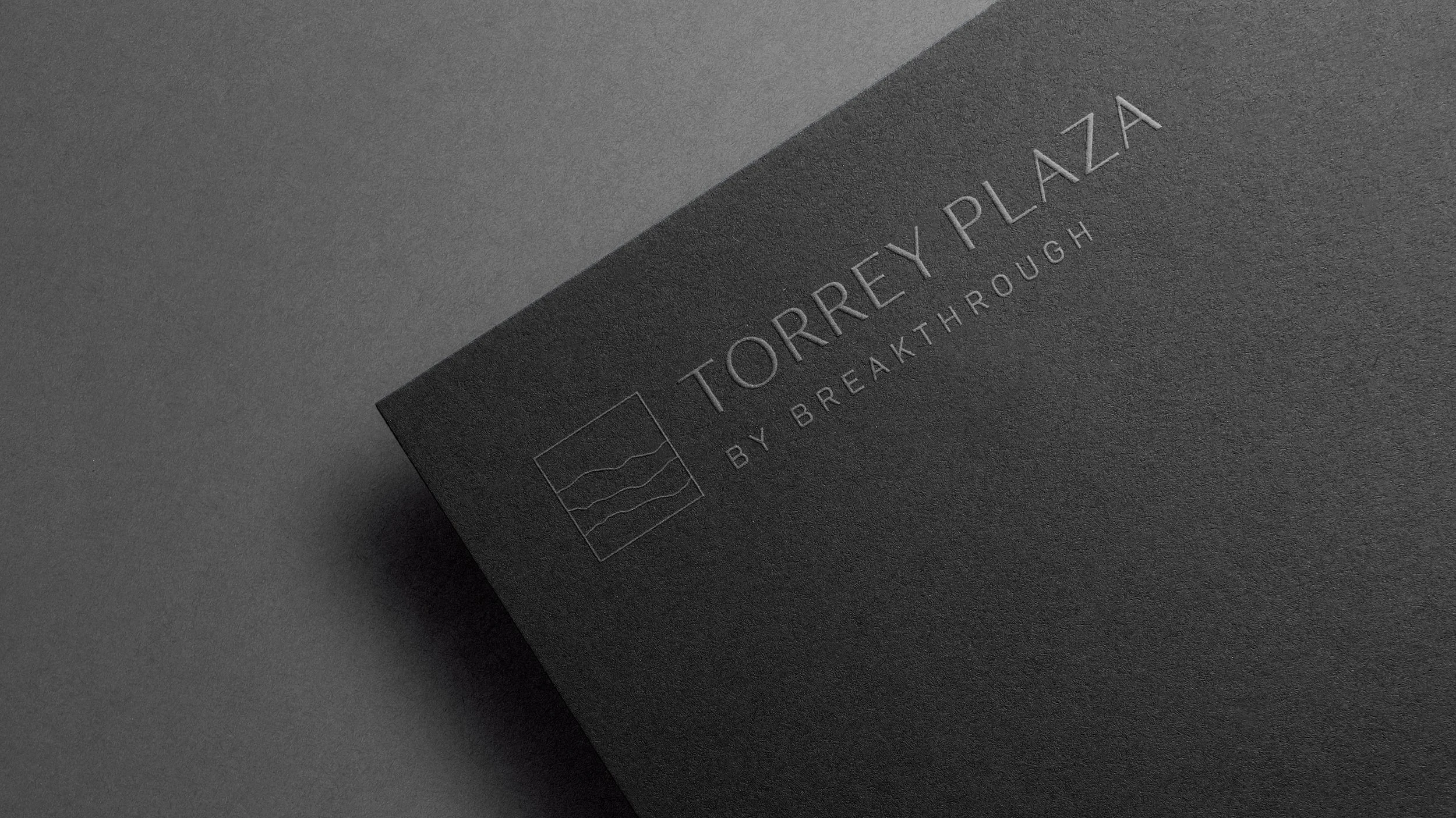 Close-up of a black business card with embossed silver lettering that reads 'TORREY PLAZA BY BREATHROUGH' and a small abstract logo.