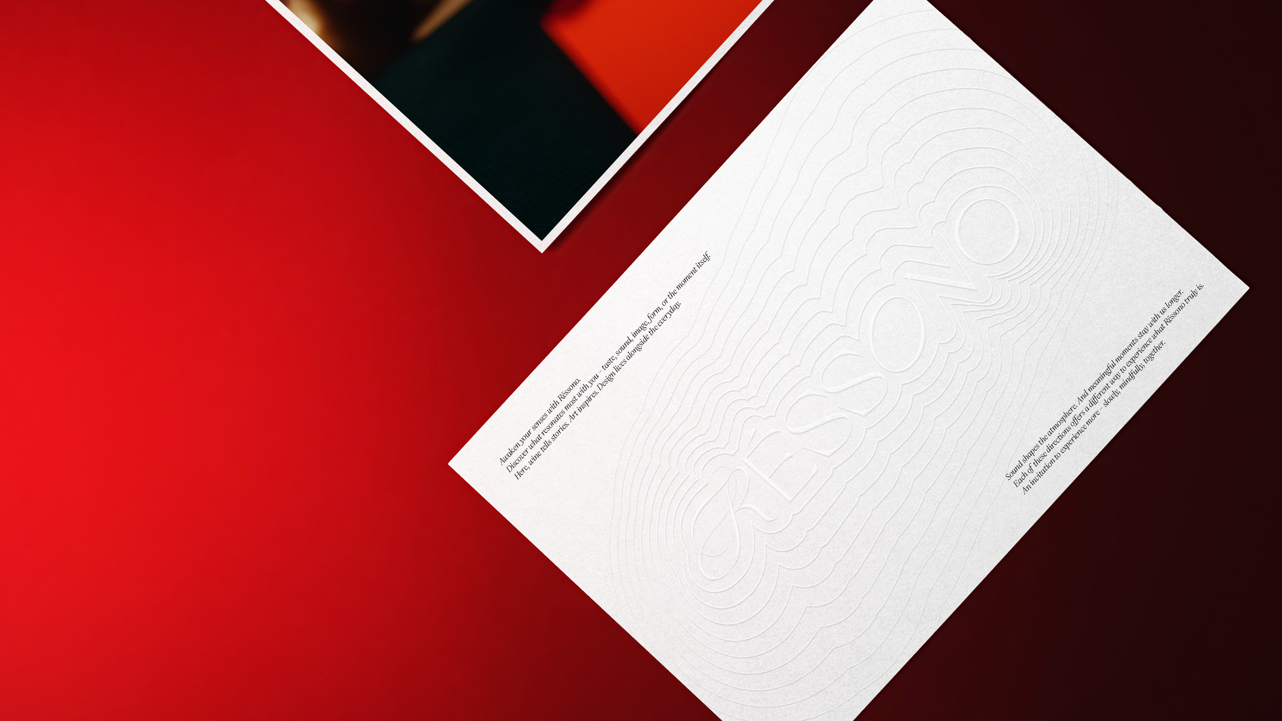 A white sheet of paper with embossed text reading "RESONANT" and additional printed text in black, placed on a dark and red background with other partially visible printed materials.