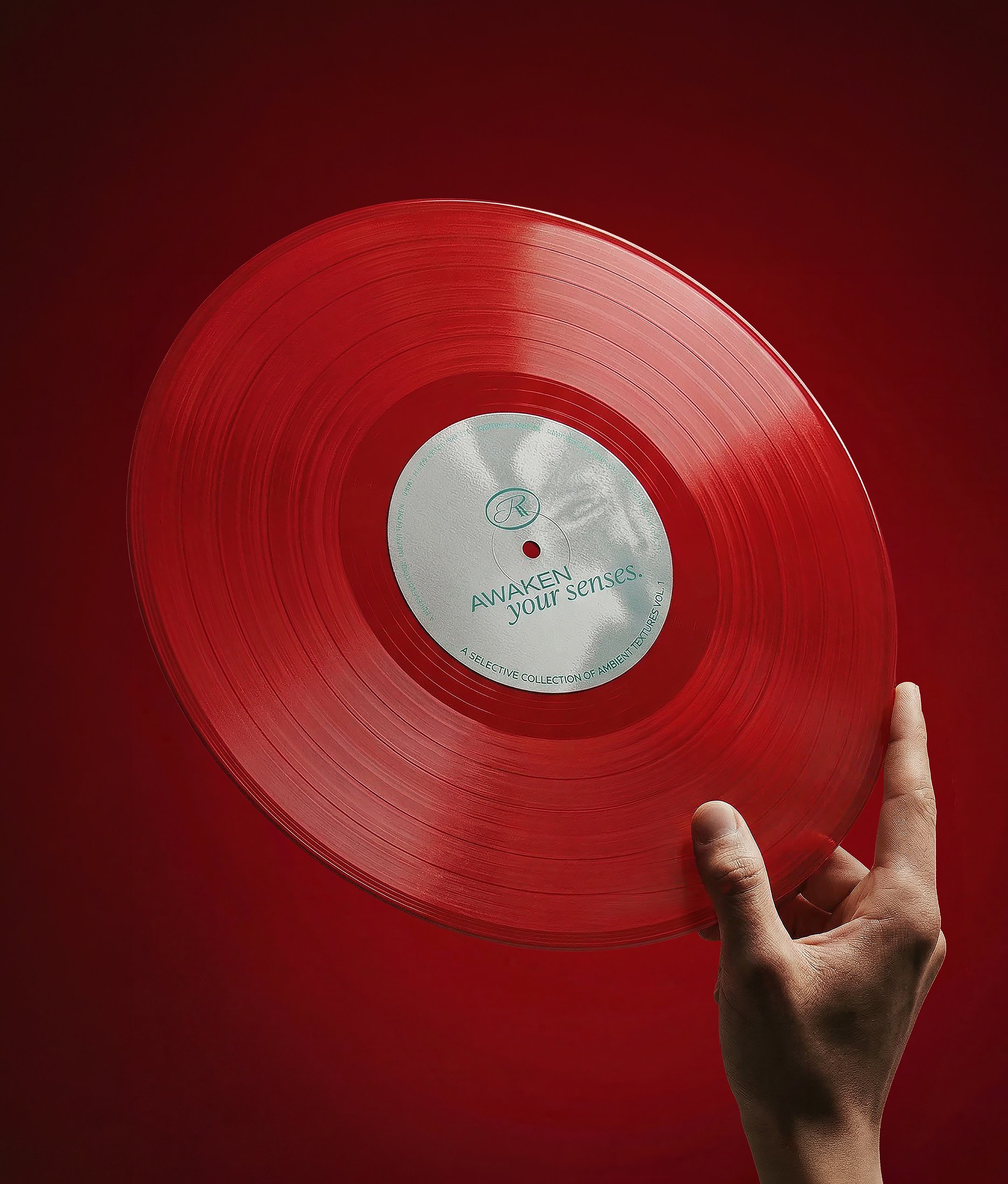 A hand holding a red vinyl record with a silver label that reads 'AWAKEN your senses.' against a red background.