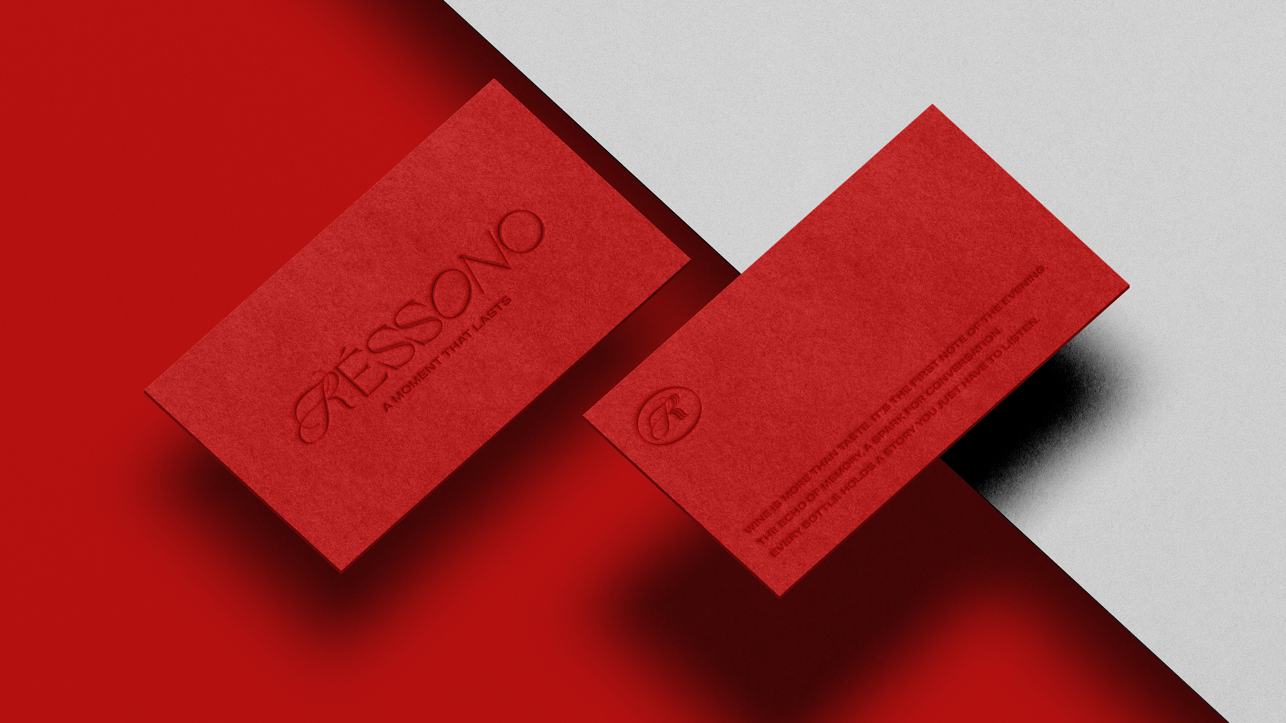 Red business cards on a background split into red and gray sections. The front card displays the text 'RESONO' and 'A MOMENT THAT LASTS' embossed, along with a logo. The back card features some smaller text including a quote about taste and a logo.