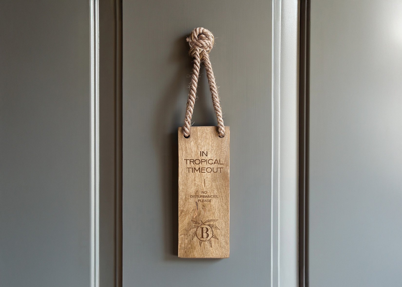 Wooden sign hanging on a door with a rope, reading "In Tropical Timeout, No Disturbances, Please" and a leaf design with the letter "B".