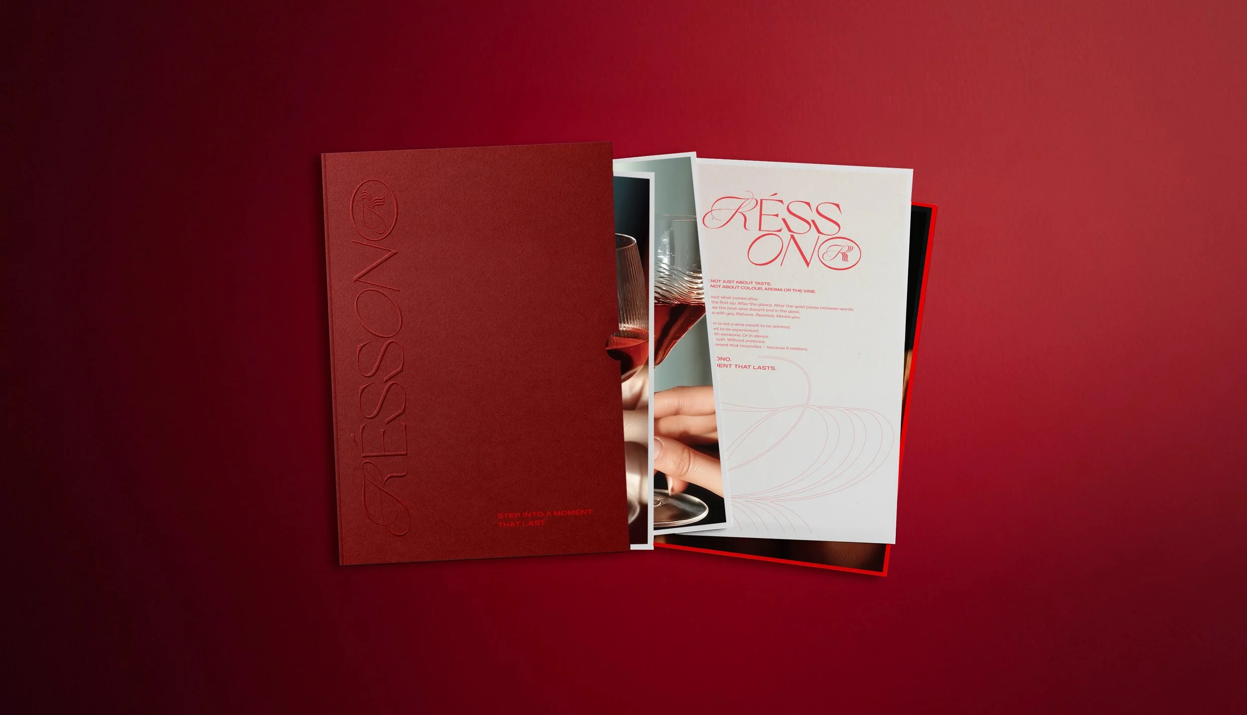 Red and white brochures or menus on a red surface, with one open showing a wine glass and a hand holding a wine glass.