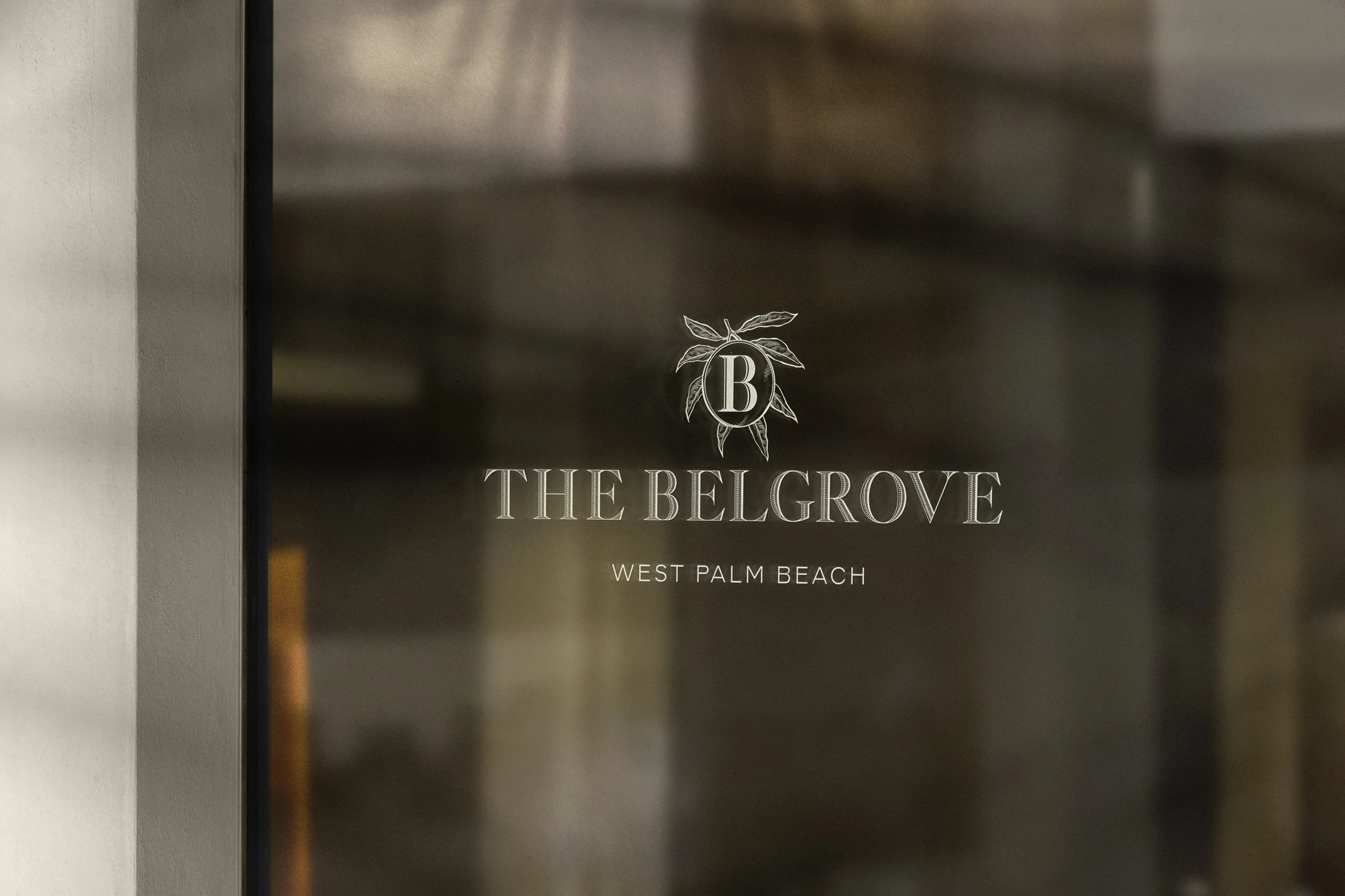 Glass door with transparent text that reads 'The Belgrave, West Palm Beach' and a decorative emblem with a letter B surrounded by leaves.