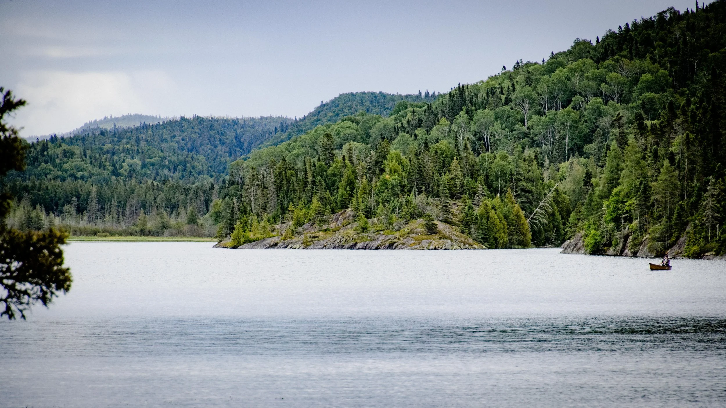 Ein ruhiger See, umgeben von bewaldeten Hügeln und Bergen, mit einem kleinen Boot auf dem Wasser.