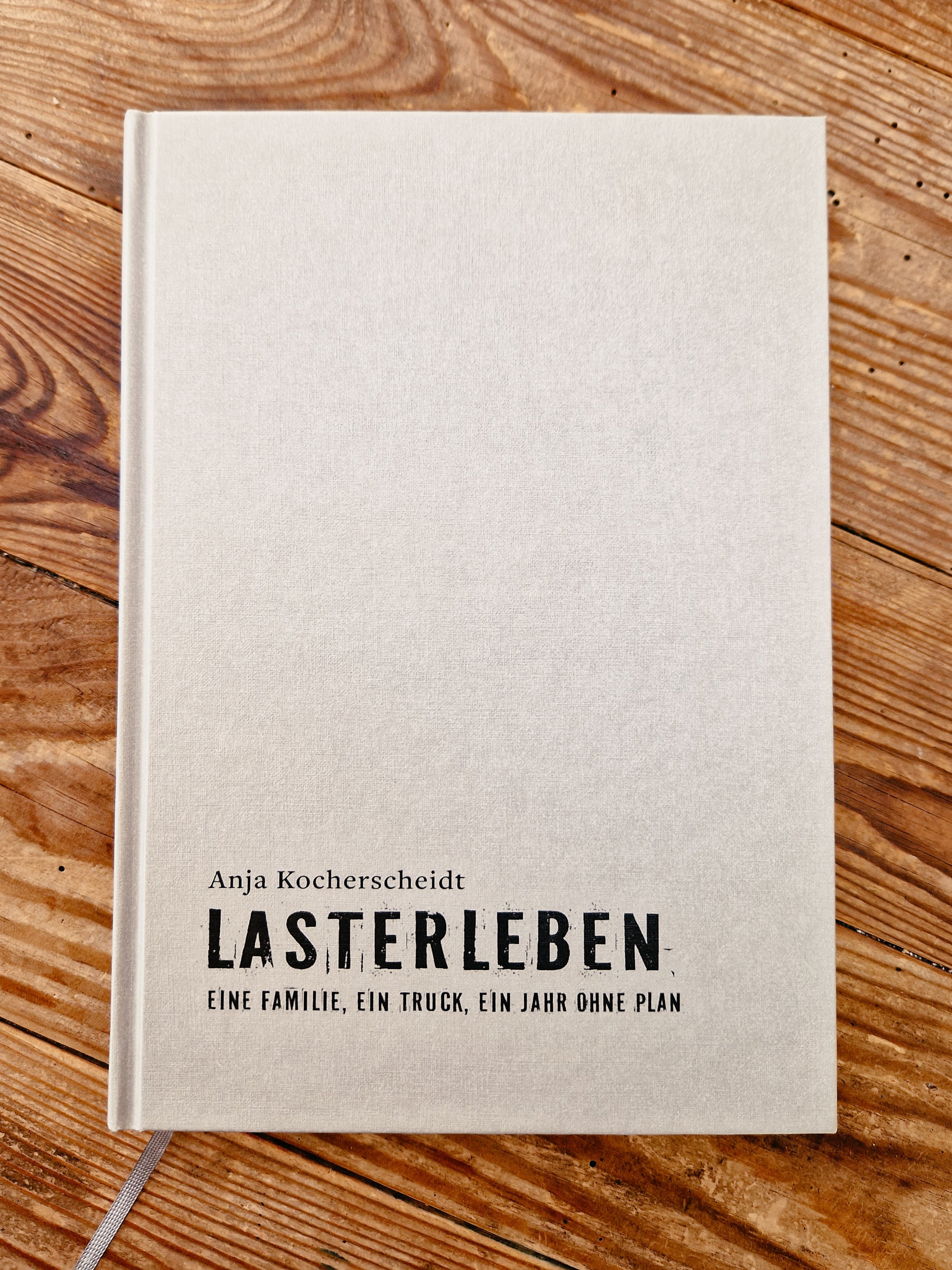 Buch "Lasterleben" ohne Schutzumschlag auf Holztisch, Titel: "LASTERLEBEN" von Anja Kocherscheidt, Untertitel: "EINE FAMILIE, EIN TRUCK, EIN JAHR OHNE PLAN".