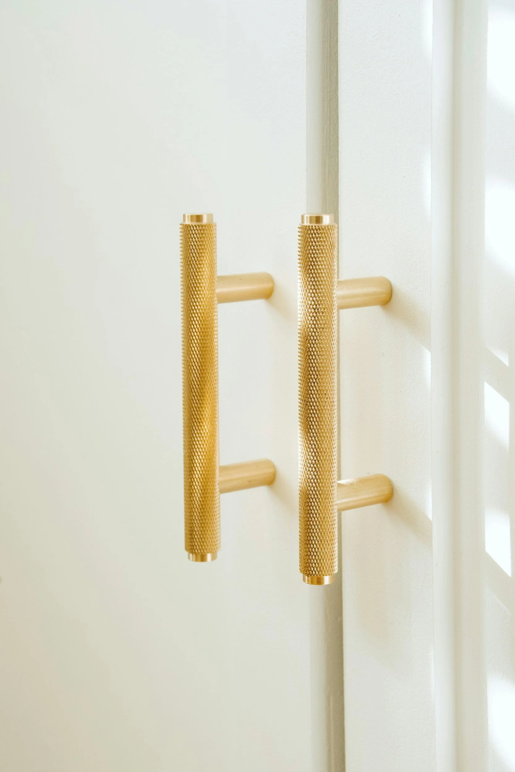 Close-up of a pair of gold-colored, textured metal handrails mounted on a light-colored wall.