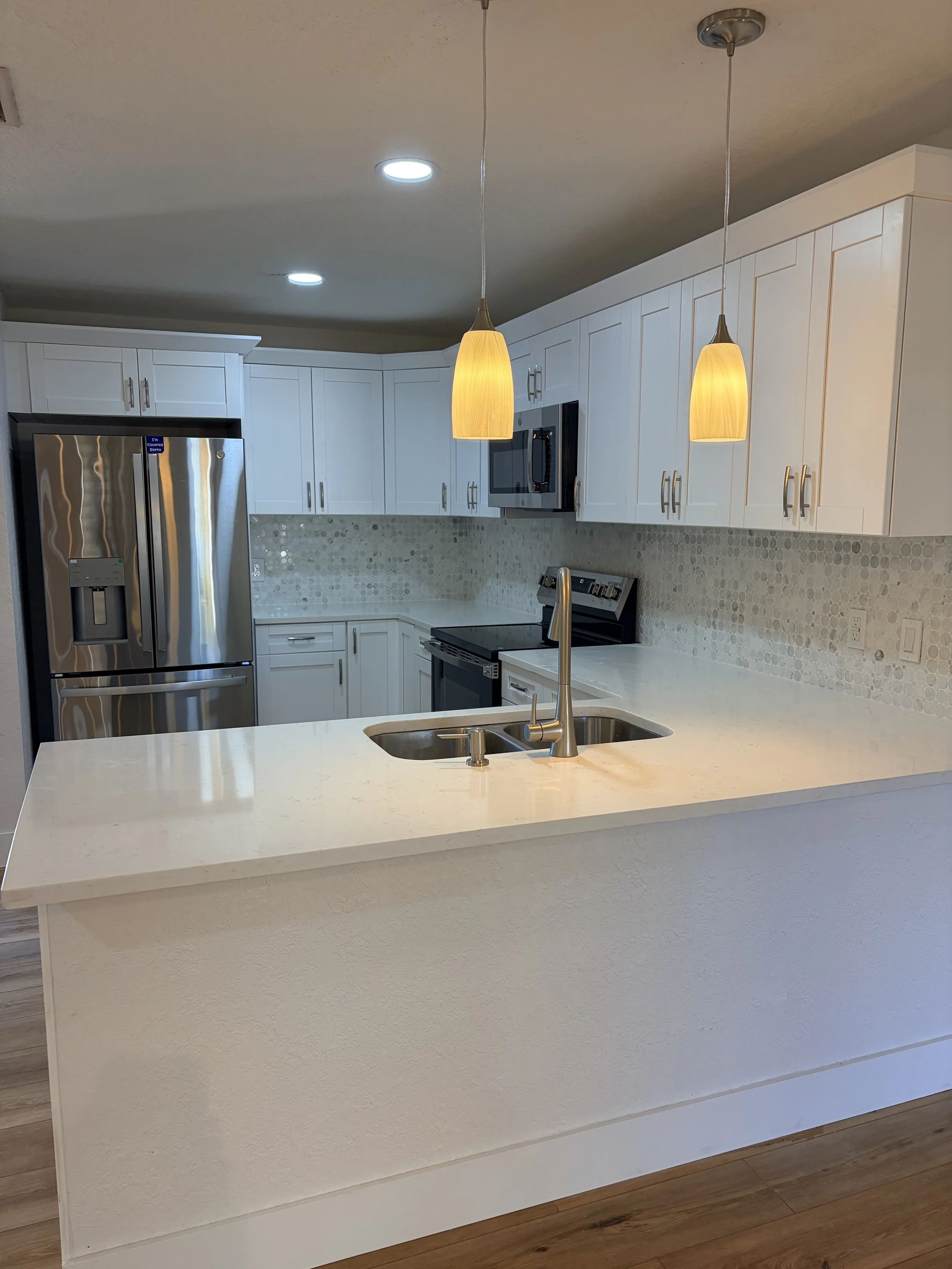 Modern kitchen with white cabinets, stainless steel appliances, a white countertop with a sink, pendant and recessed lighting, and a wood floor.