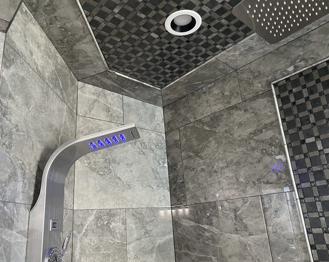 A modern shower with gray marble tiles, a built-in overhead showerhead, and a sleek, curved digital control panel.