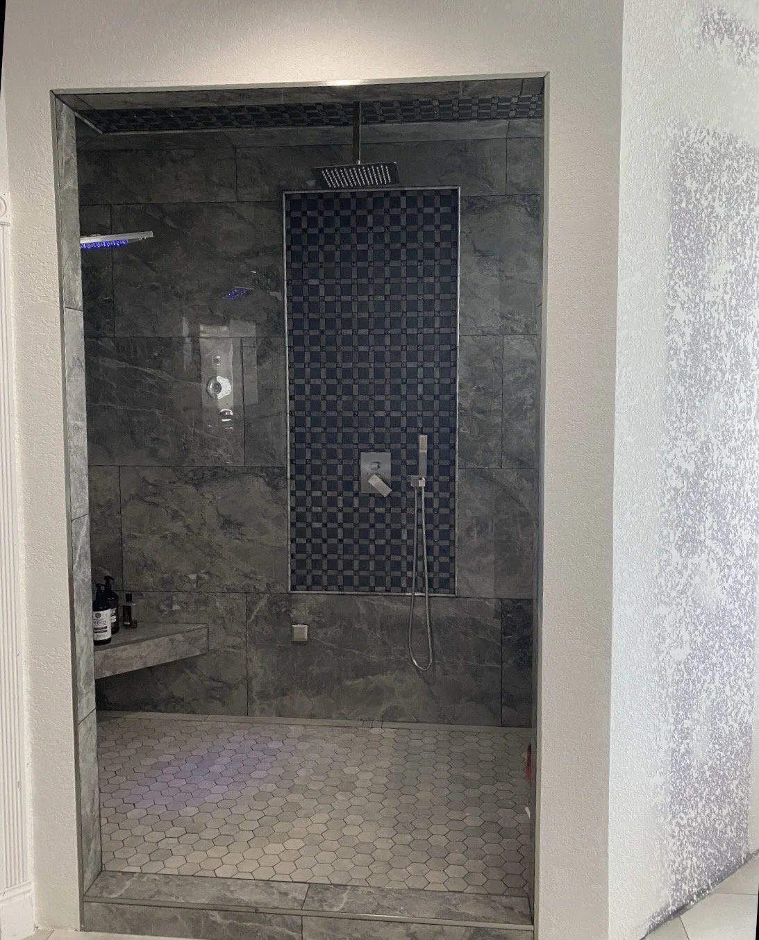 A walk-in shower with gray marble tiles on the walls and hexagonal tiles on the floor, featuring a rain showerhead and handheld shower.