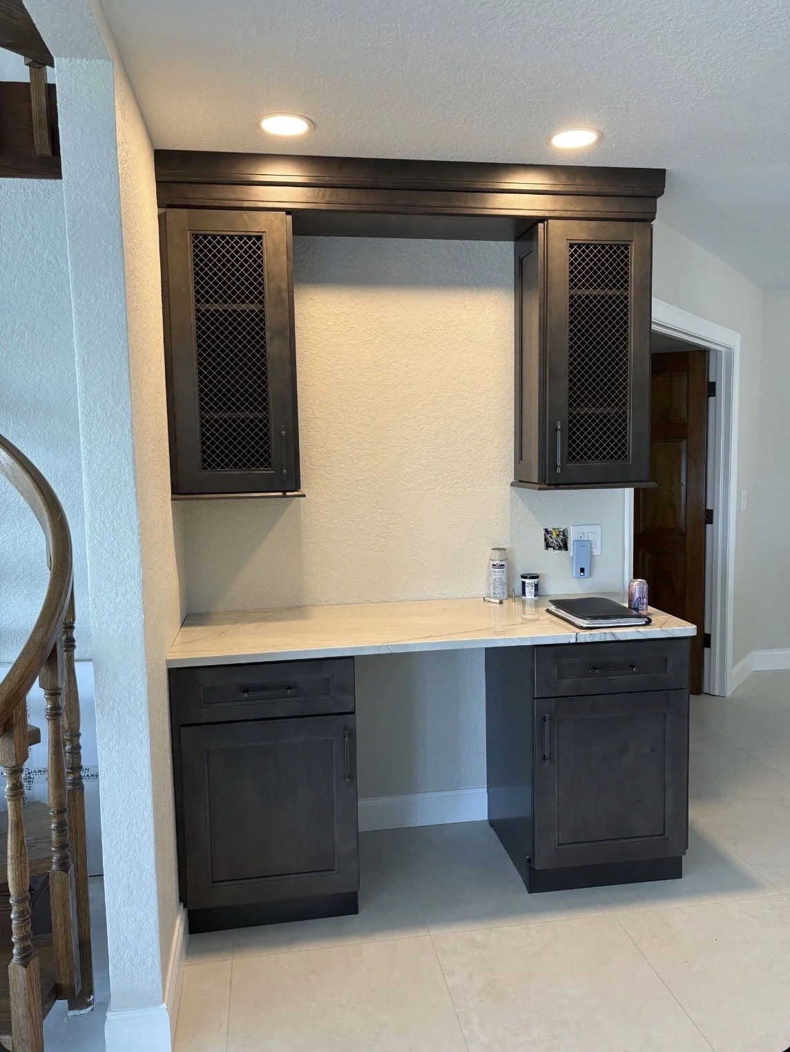 Kitchen or bar area with dark wooden cabinets, a light-colored countertop, and a wall space for a appliances or decorations, with some cans and a laptop on the counter.