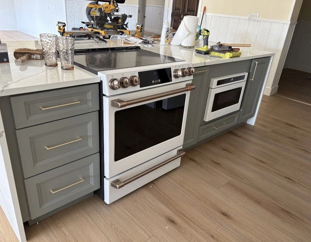 Kitchen countertop with two ovens, a new power saw, glasses, paper towels, cleaning spray, tape measure, and tools in a home renovation setting.