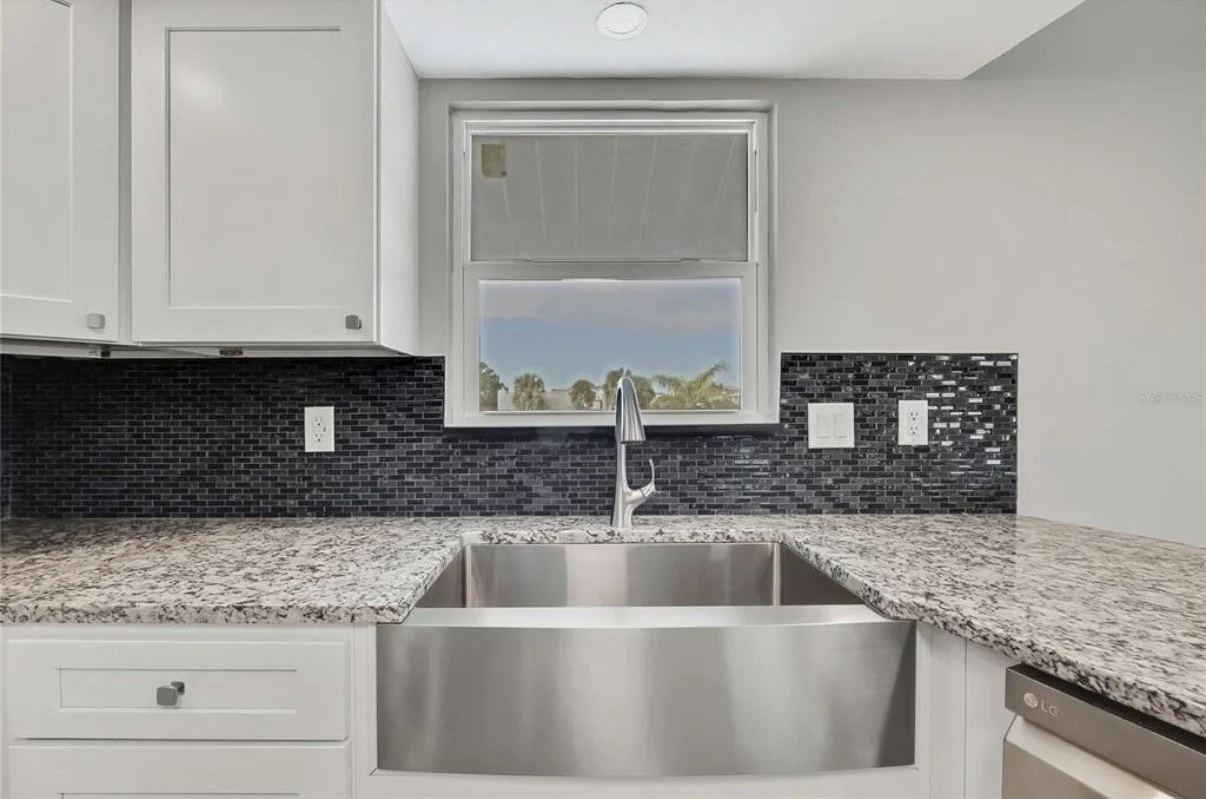 Kitchen with granite countertops, white cabinets, black mosaic tile backsplash, stainless steel sink, and a window above the sink.