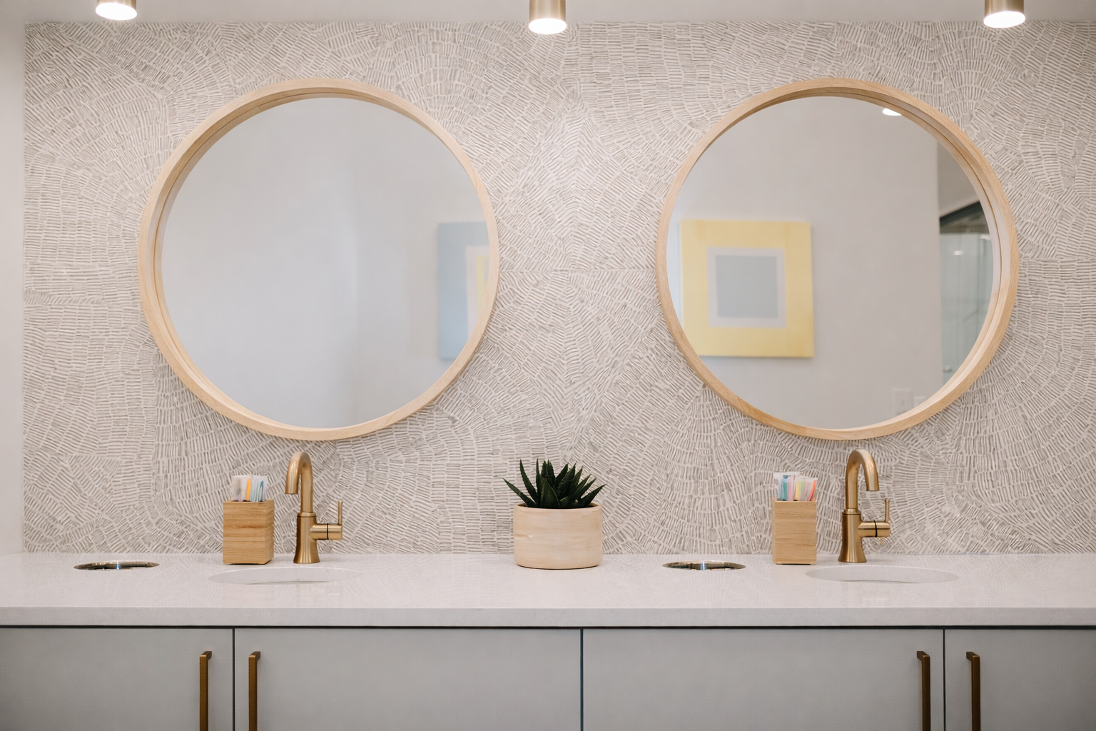 Modern bathroom double vanity with two round mirrors, gold faucets, wooden soap dispensers, a green potted plant, and textured wall background