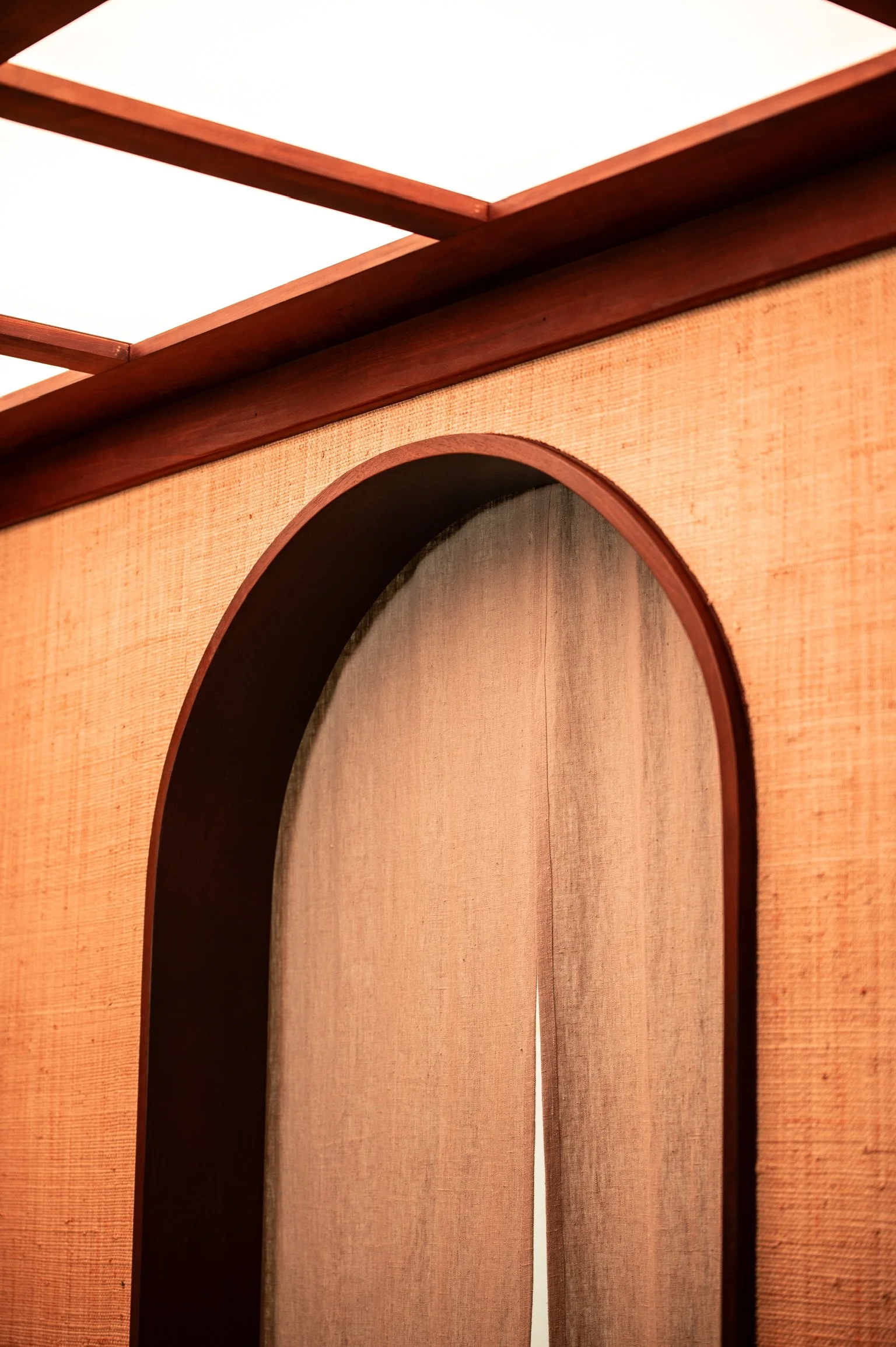 Close-up of a wooden room divider with an arched cutout and light-colored fabric backing, partly showing a mirror reflection.