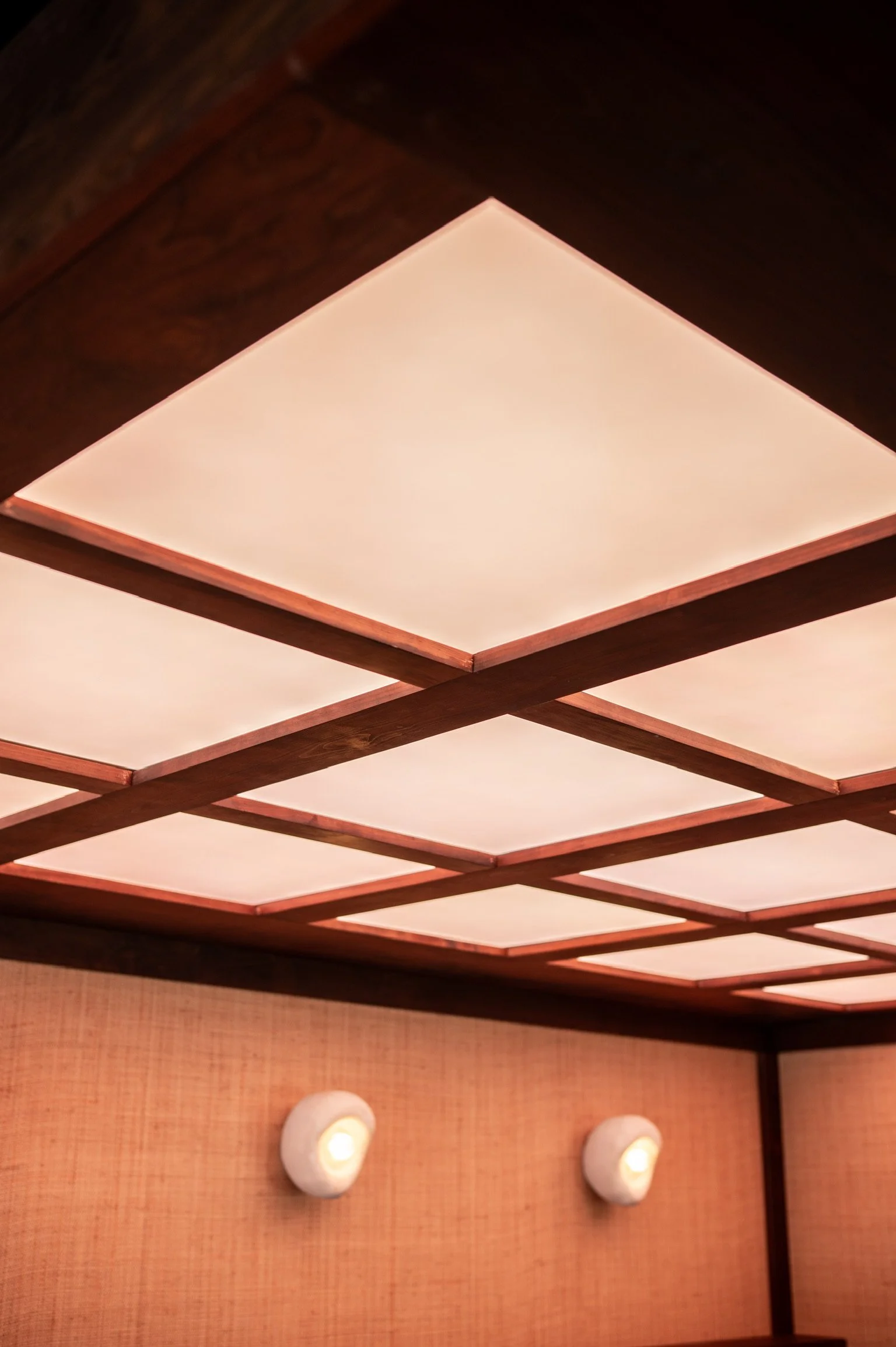 Ceiling with wooden frame and backlit panels, two wall-mounted lights below, interior decor.