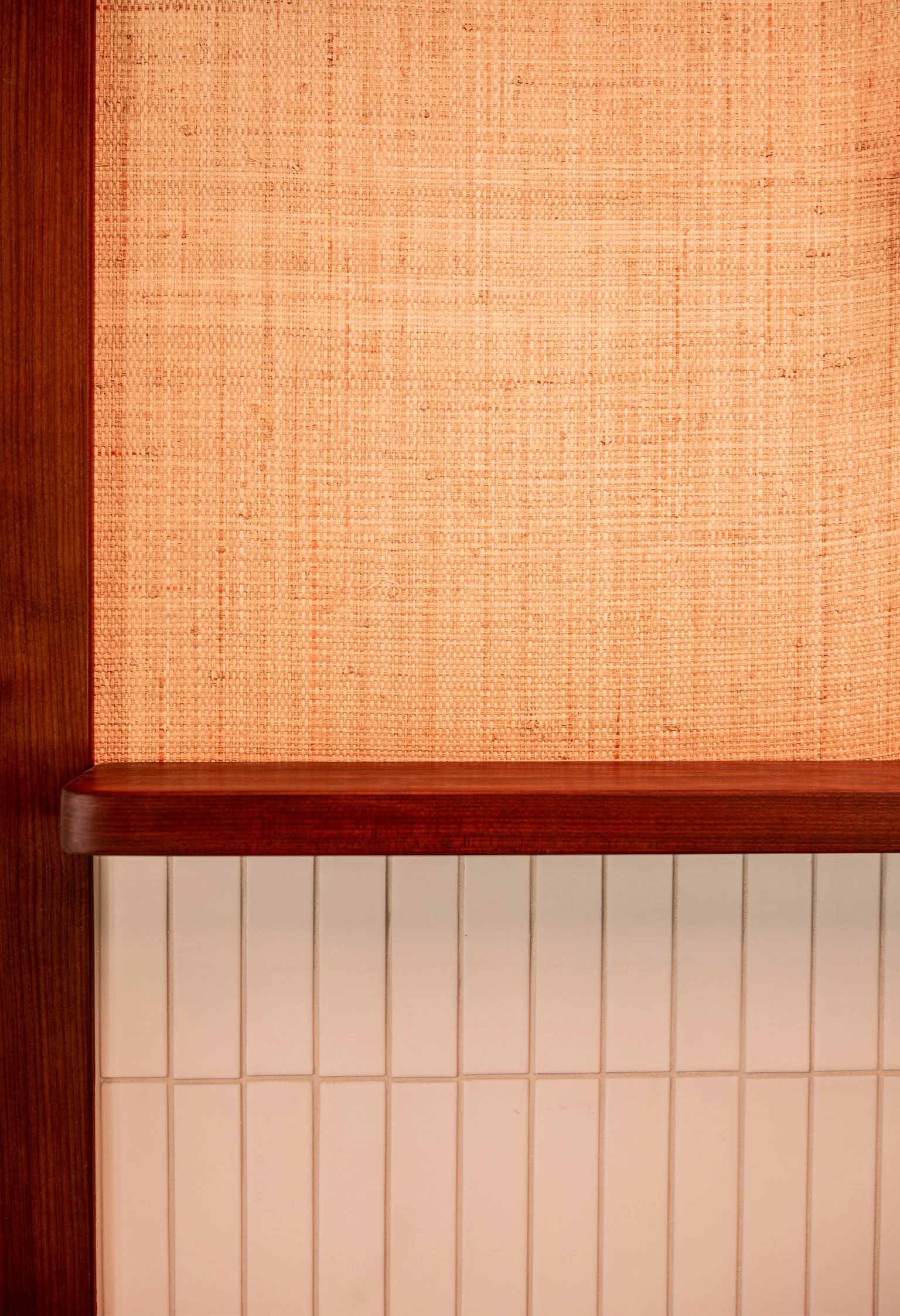 A wooden wall with a large, peach-colored woven fabric hanging in the center, framed by dark wooden trim on the left and bottom, with white tiled walls below.
