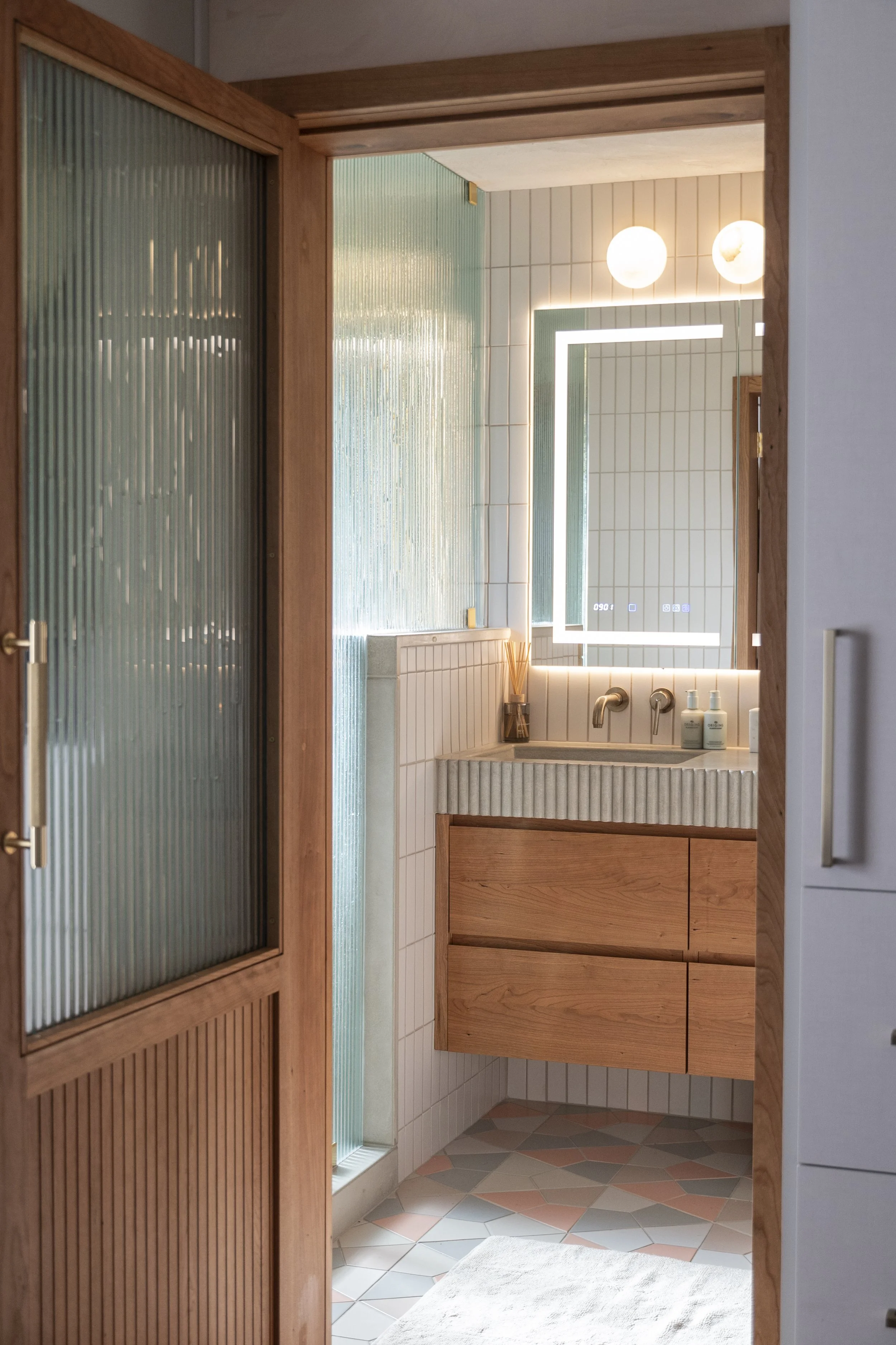 Modern bathroom with a wooden vanity, striped countertop, illuminated mirror, and soft lighting.
