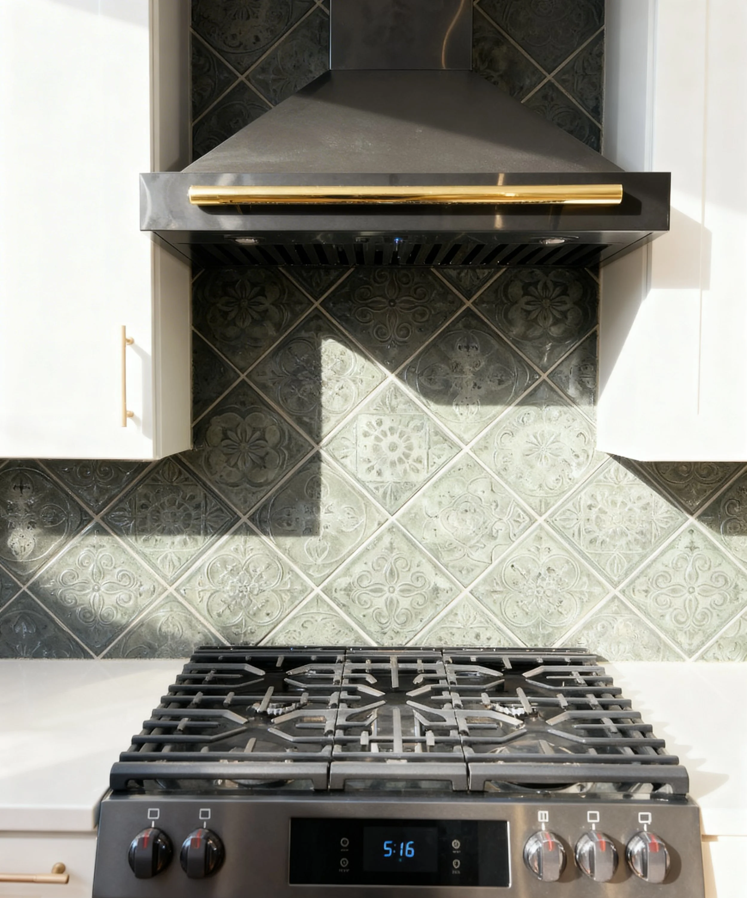 View of a kitchen stovetop against a patterned tile backsplash, with a black range hood above and white cabinetry on either side.