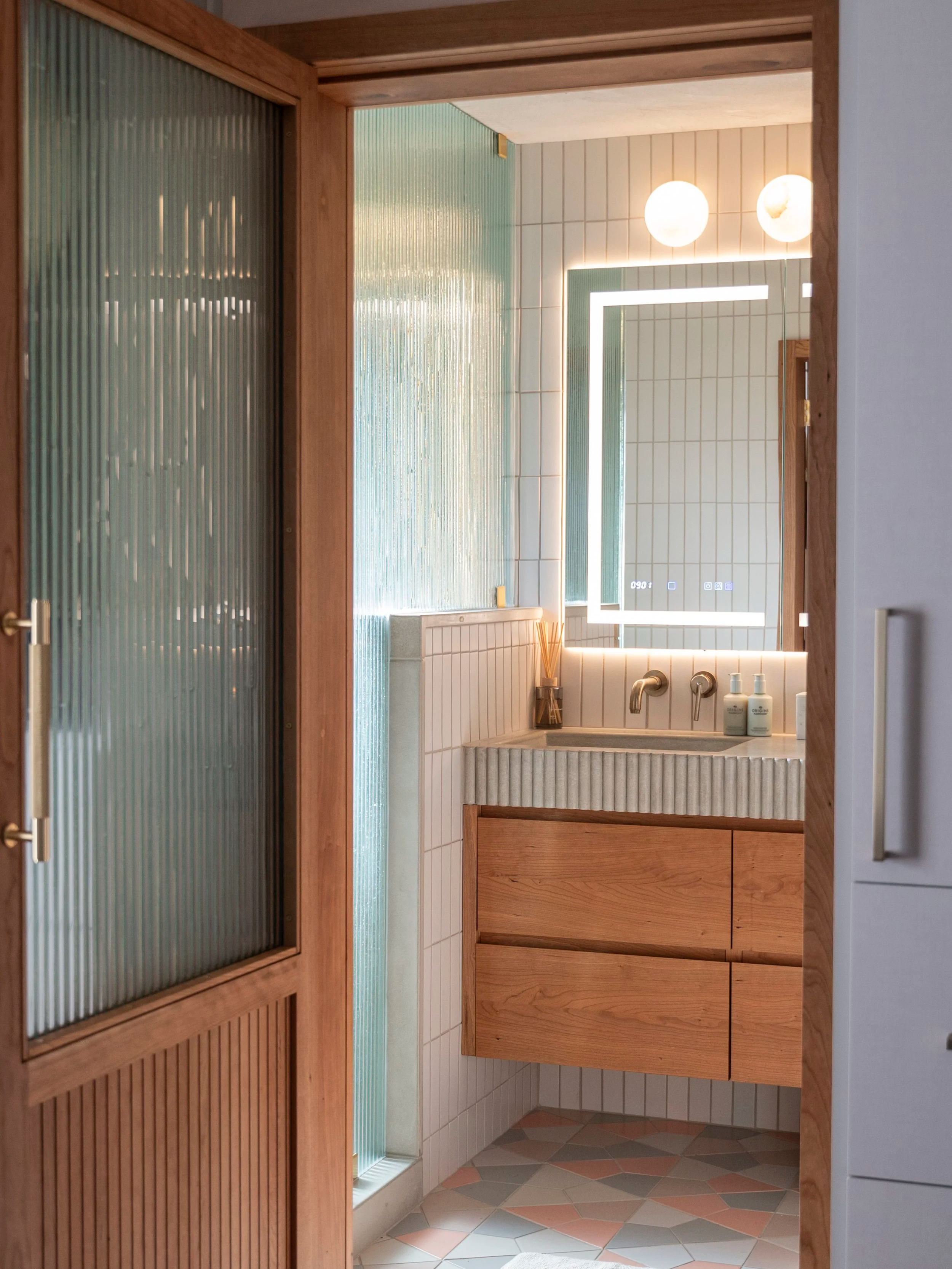 Modern bathroom with a illuminated rectangular mirror, wooden vanity, and textured glass shower door.