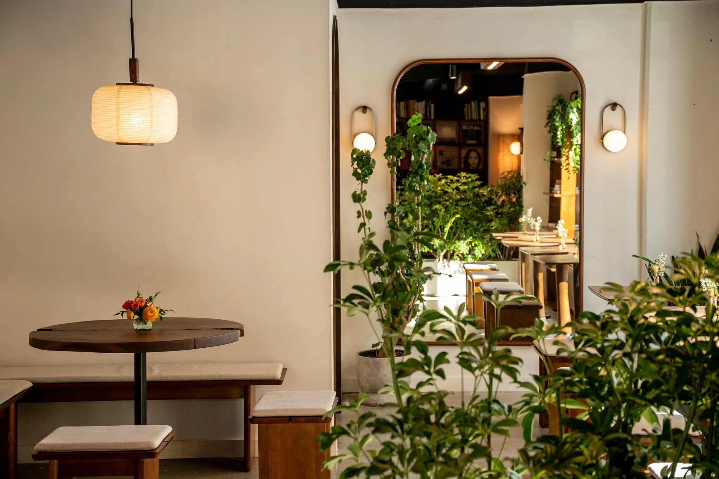 Interior of a cozy cafe or restaurant with wooden furniture, greenery, and soft lighting from hanging and wall-mounted lamps.