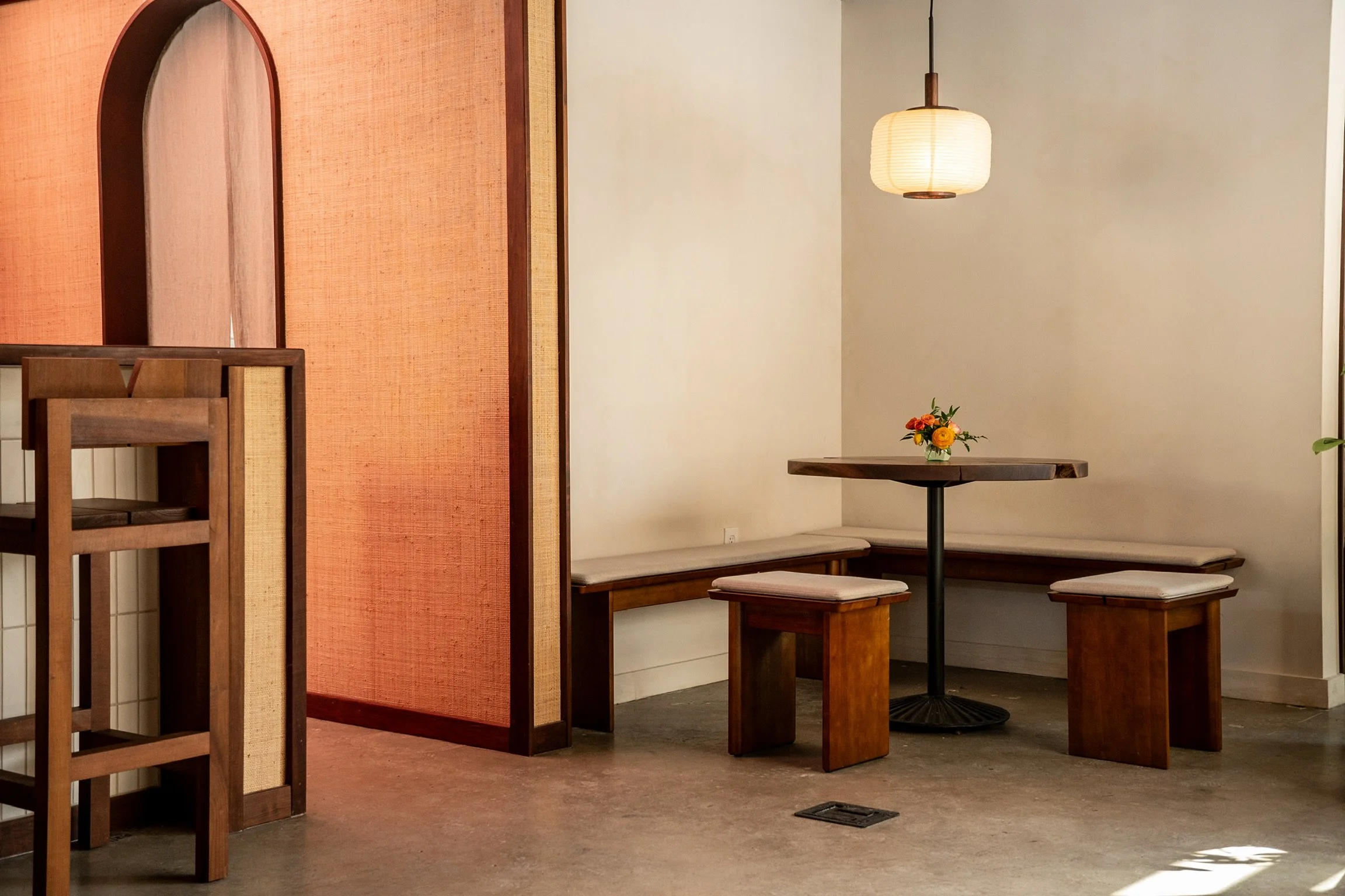 Interior of a restaurant with wooden furniture, a table with a small flower arrangement, hanging light, and a corner seating area with benches.