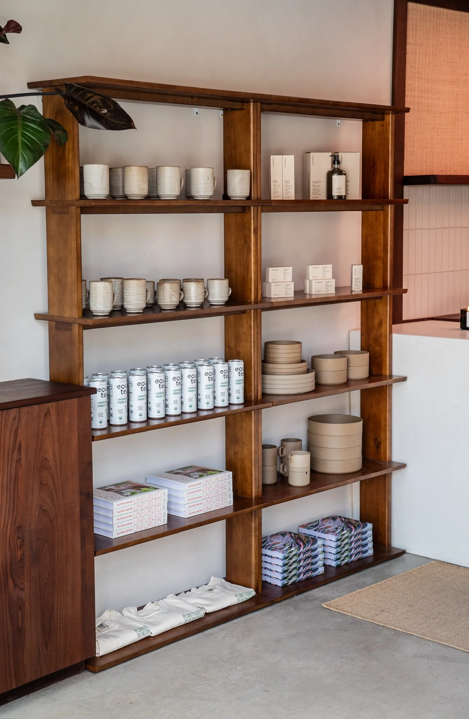 Wooden bookshelf with cups, boxes, and ceramics, located in a store or studio with a beige rug on a concrete floor.