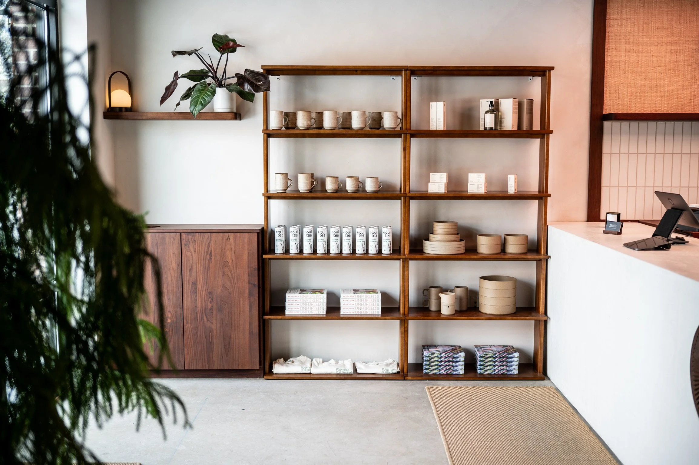 Wooden shelf with beige mugs, white boxes labeled 'equi tea,' stacks of paper or cloth, and other small items inside a cozy cafe or store with a white wall background.