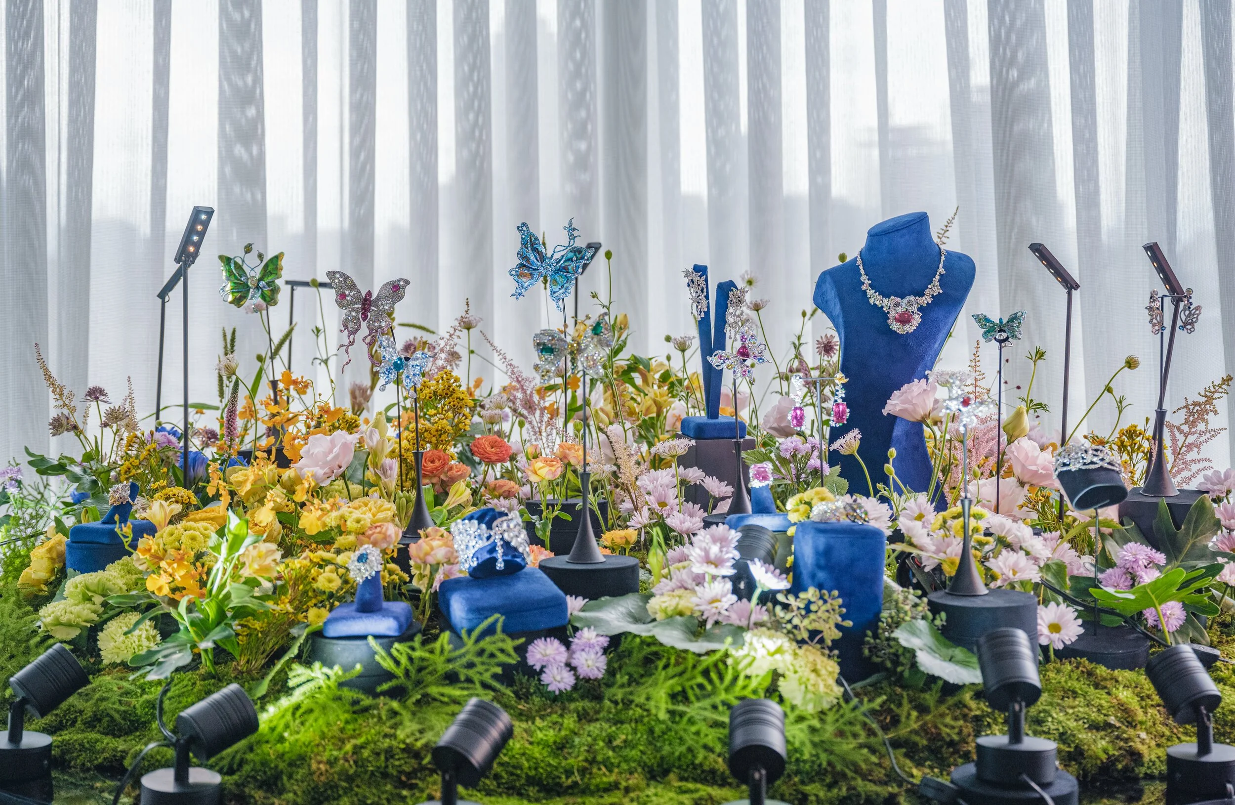 Jewelry display with floral backdrop featuring necklaces, rings, and butterfly decorations in a garden setting.