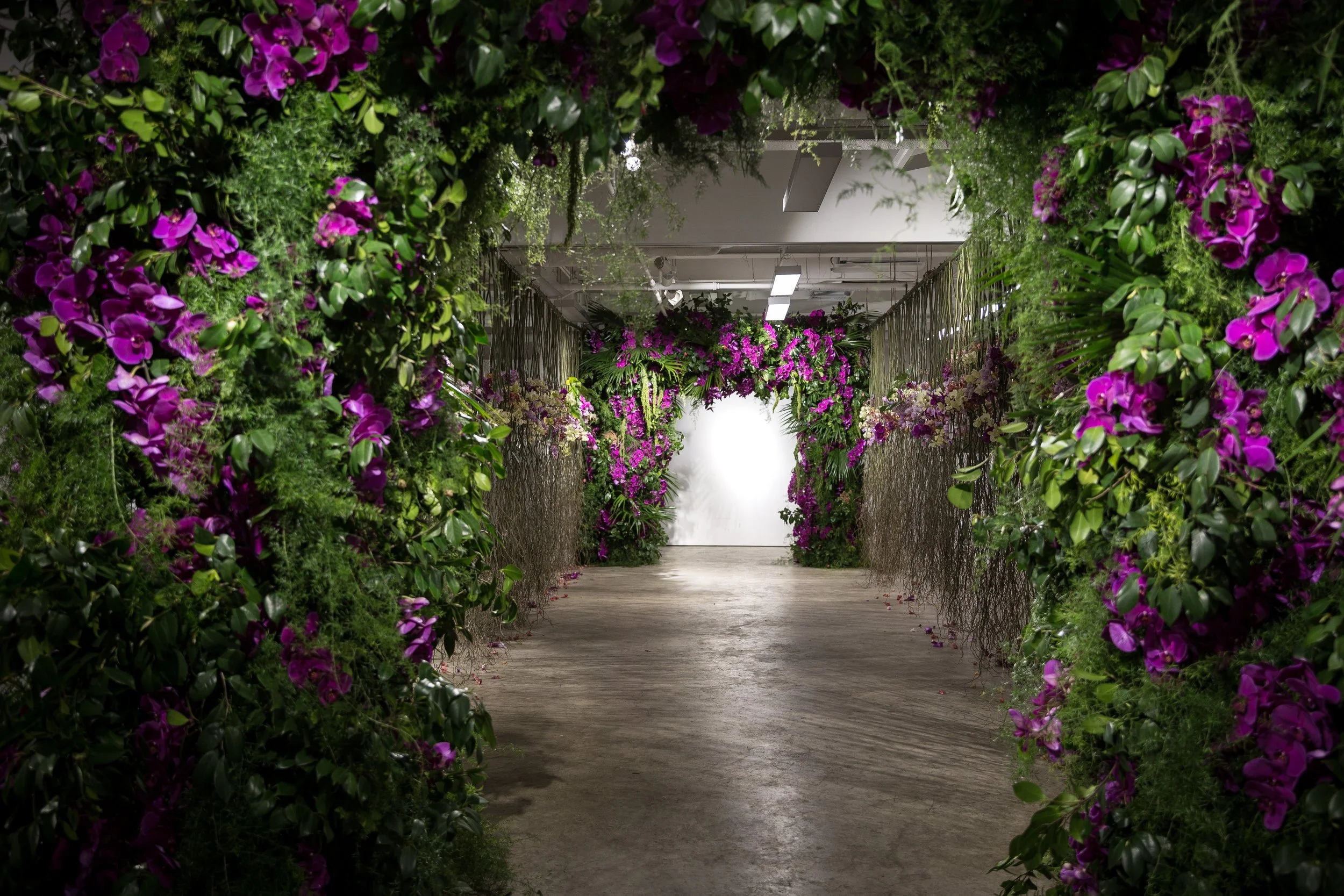 Indoor hallway adorned with lush greenery and vibrant purple flowers, creating a natural archway effect.