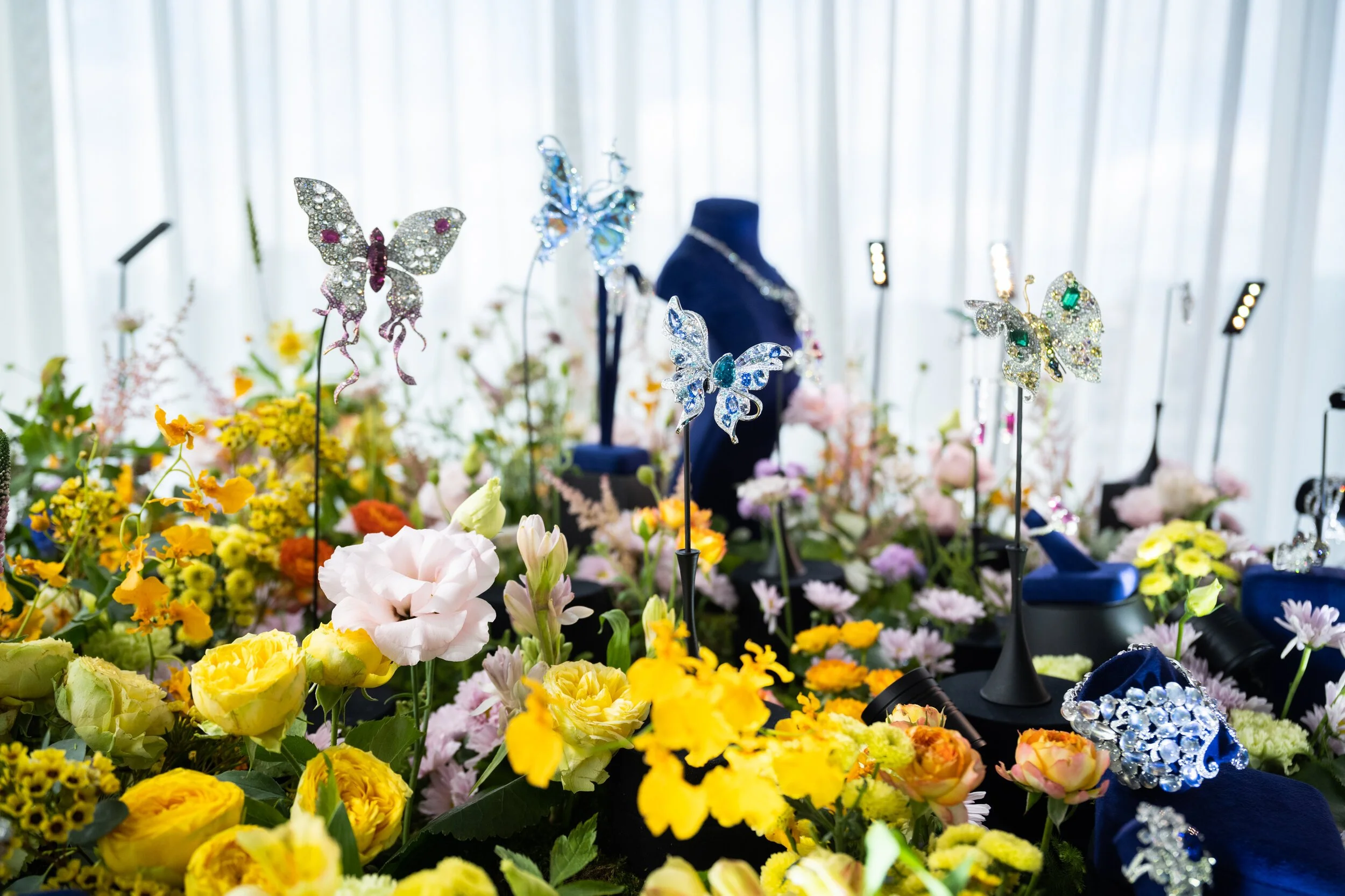 Colorful floral arrangement with jeweled butterfly decorations and jewelry on display.